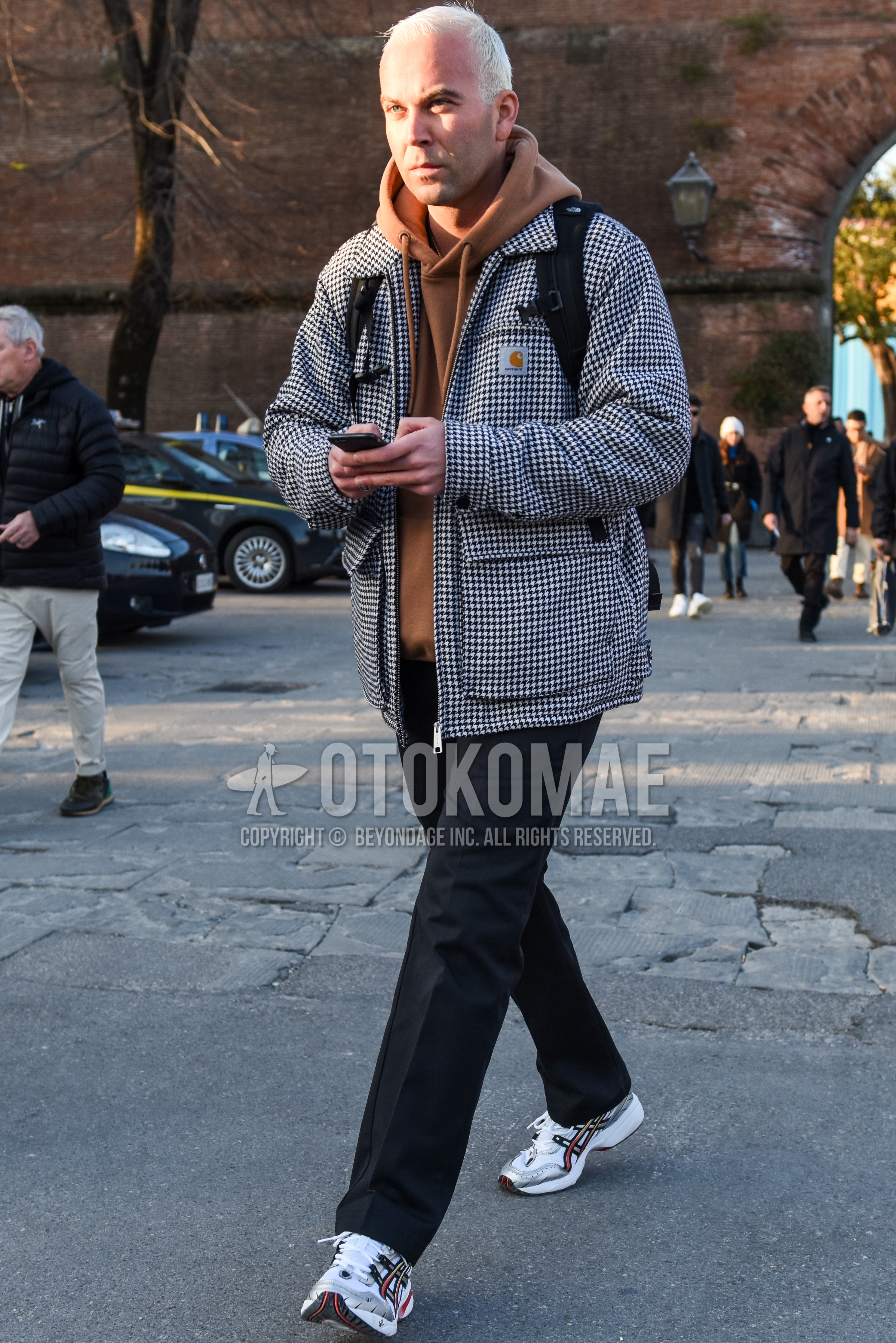 Men's autumn winter outfit with white black check coverall, beige plain hoodie, gray plain slacks, white low-cut sneakers.