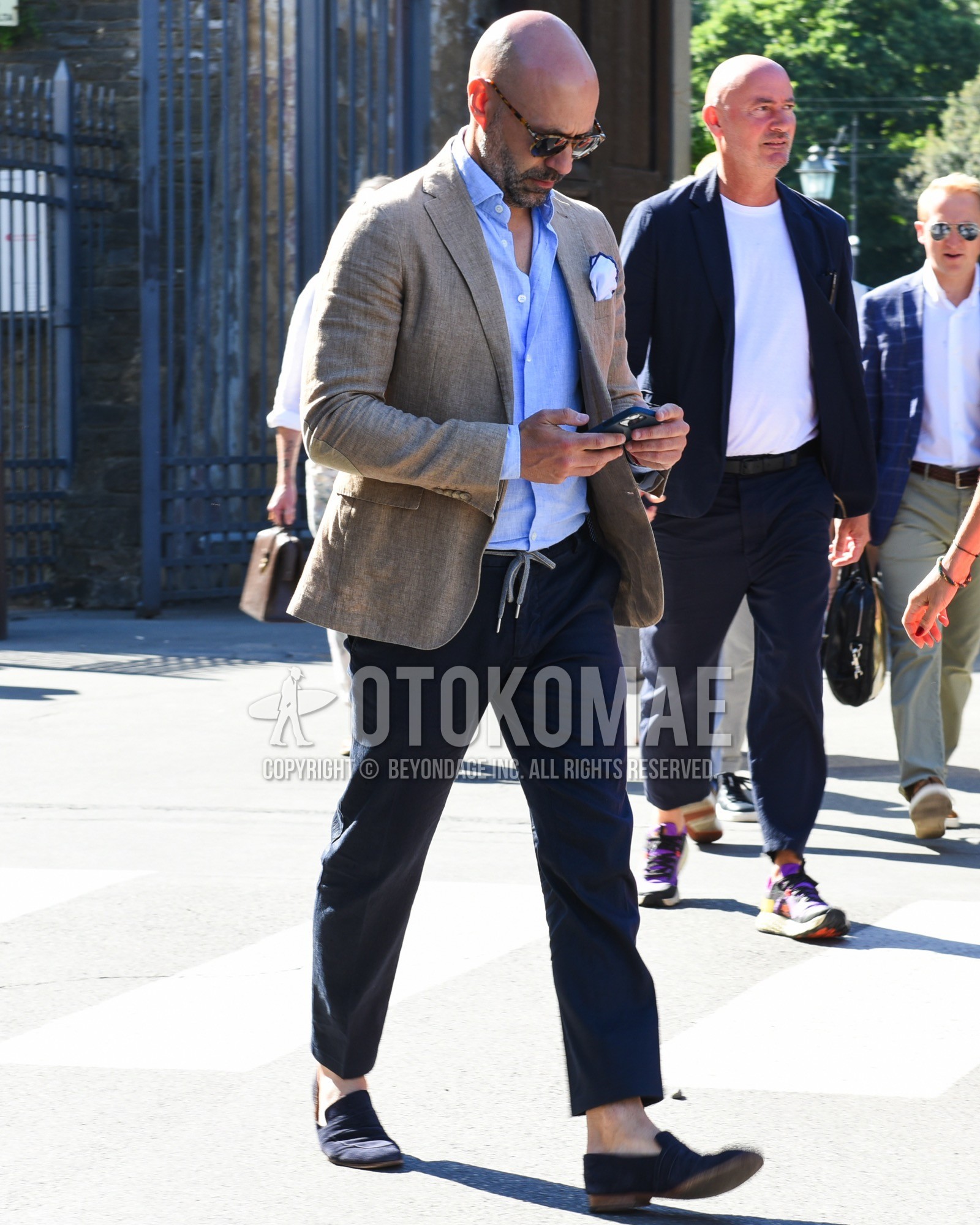 Men's spring summer outfit with brown tortoiseshell sunglasses, gray plain tailored jacket, blue plain shirt, navy plain easy pants, navy  loafers leather shoes.