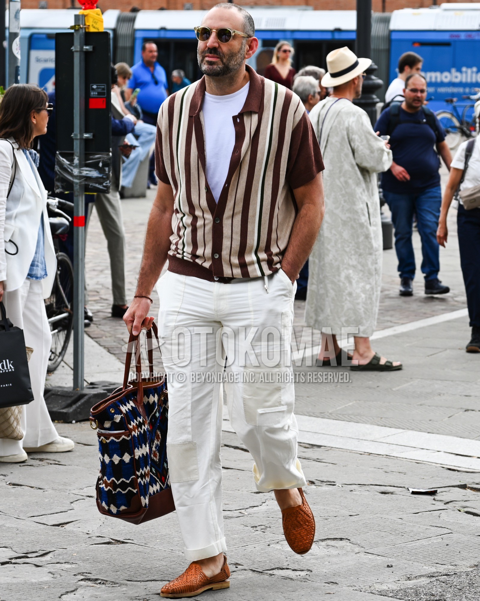 Men's spring summer outfit with black plain sunglasses, brown stripes cardigan, white plain t-shirt, white plain cargo pants, brown  loafers leather shoes, black bag tote bag.