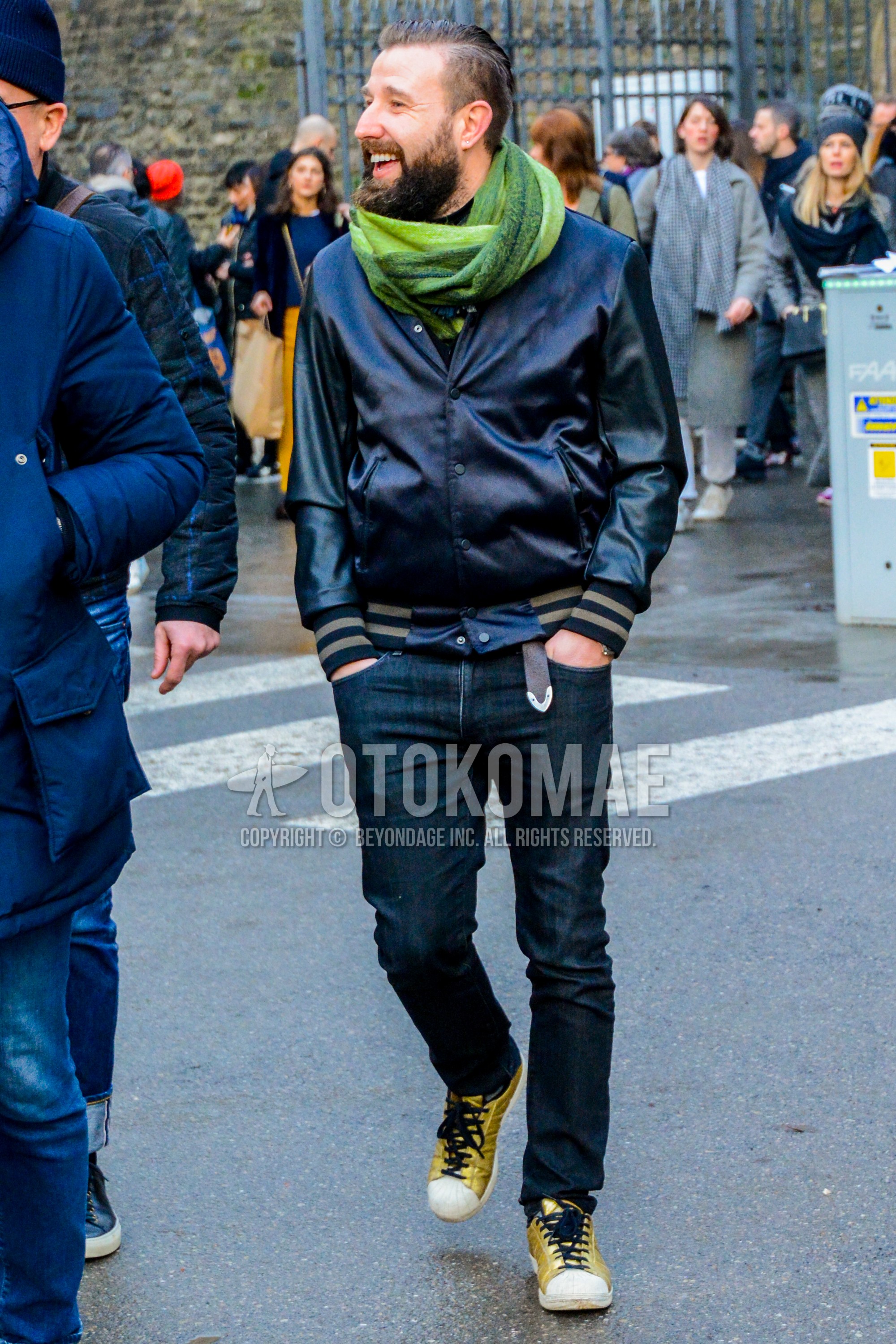 Men's winter outfit with green plain scarf, black plain stadium jacket, black plain denim/jeans, yellow low-cut sneakers.