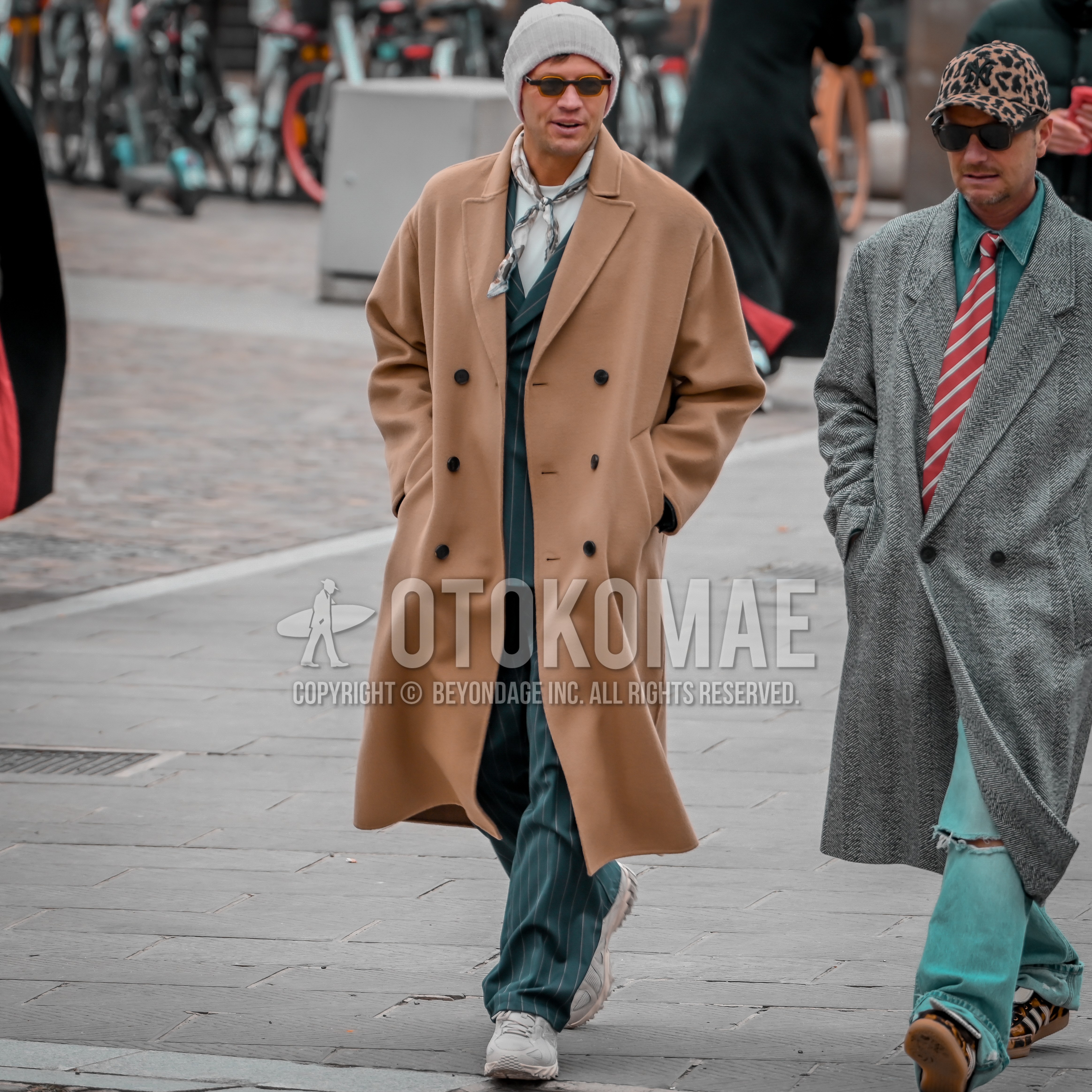 Men's autumn winter outfit with gray plain knit cap, black plain sunglasses, white blue beige scarf bandana/neckerchief, beige plain chester coat, gray low-cut sneakers, green stripes casual setup.