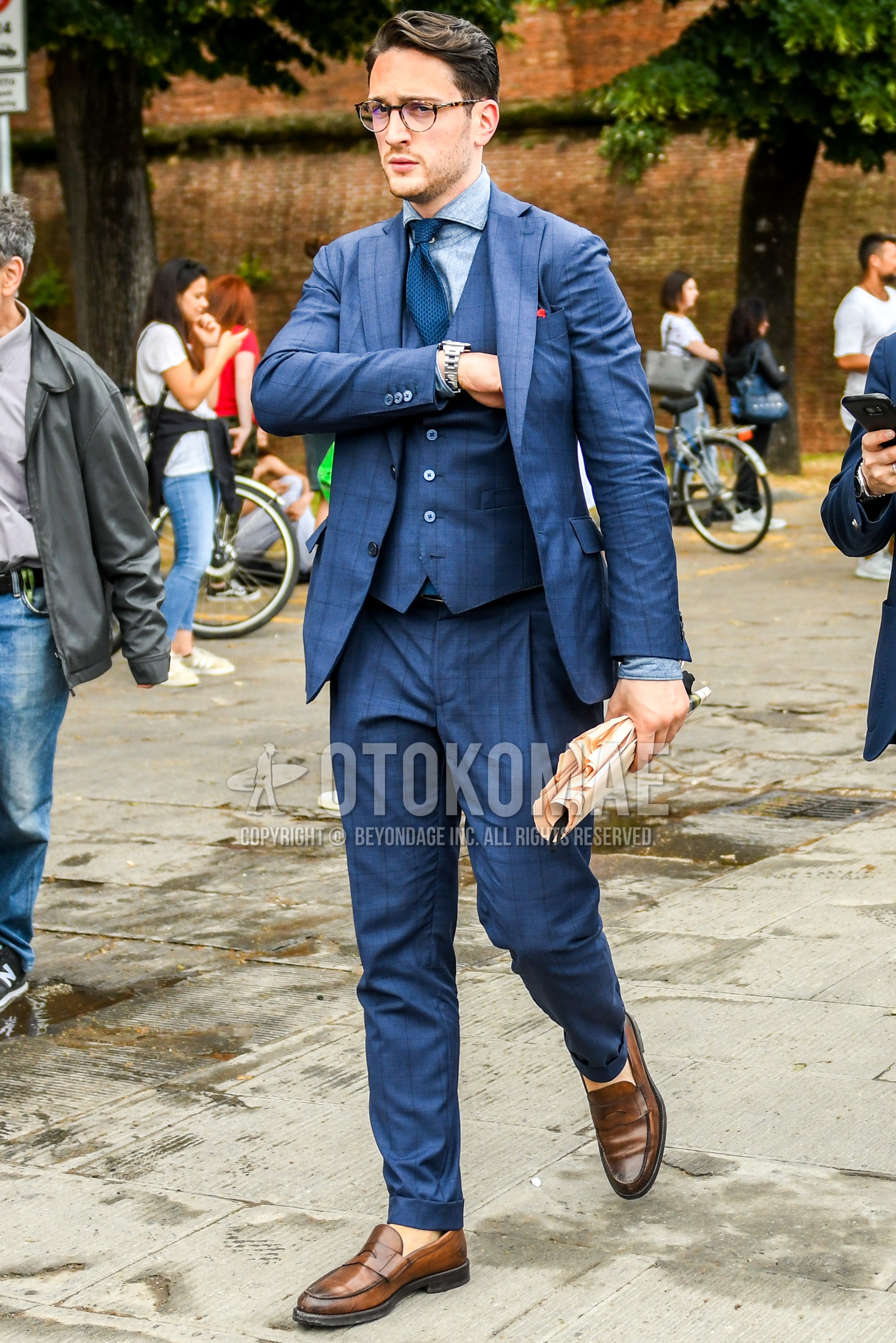 Men's spring autumn outfit with beige tortoiseshell glasses, light blue plain denim shirt/chambray shirt, brown coin loafers leather shoes, blue check three-piece suit, blue necktie necktie.
