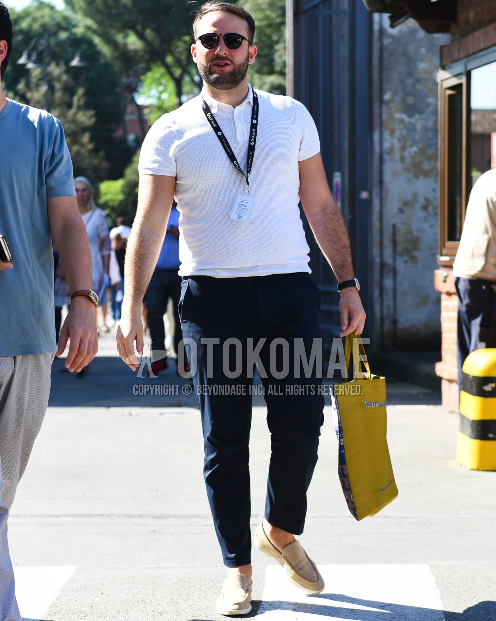 Men's spring summer outfit with black plain sunglasses, white plain polo shirt, navy plain chinos, beige slip-on sneakers, yellow one point tote bag.