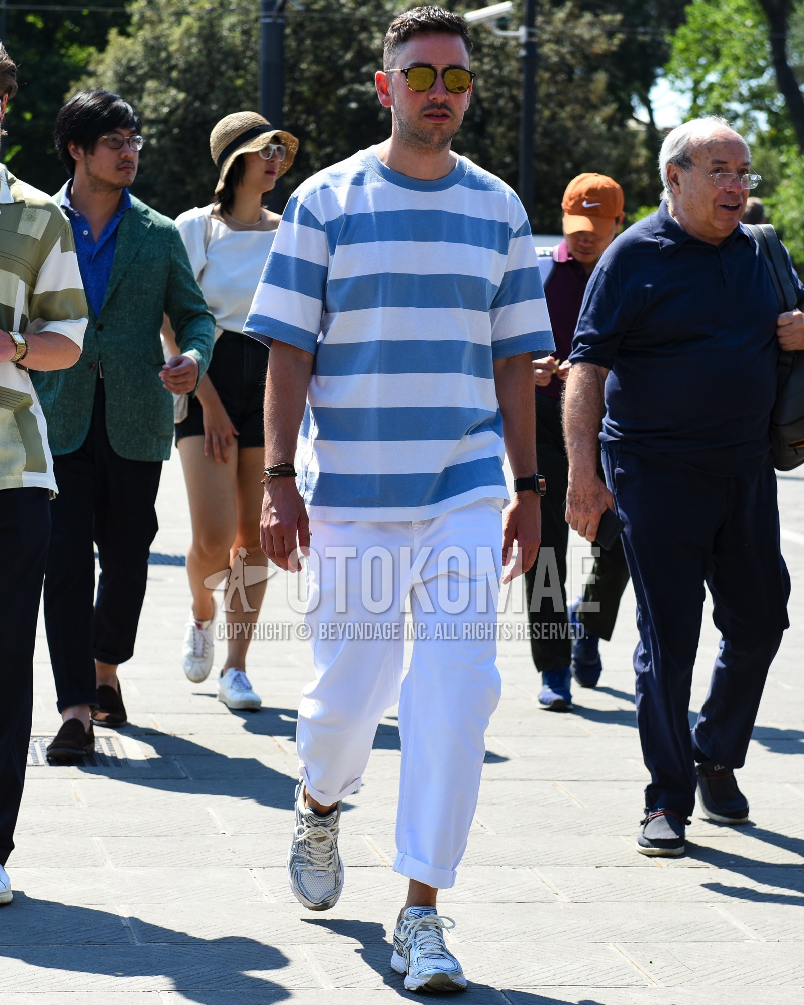 Men's spring summer outfit with black plain sunglasses, brown tortoiseshell sunglasses, blue white horizontal stripes t-shirt, white plain cotton pants, silver low-cut sneakers.