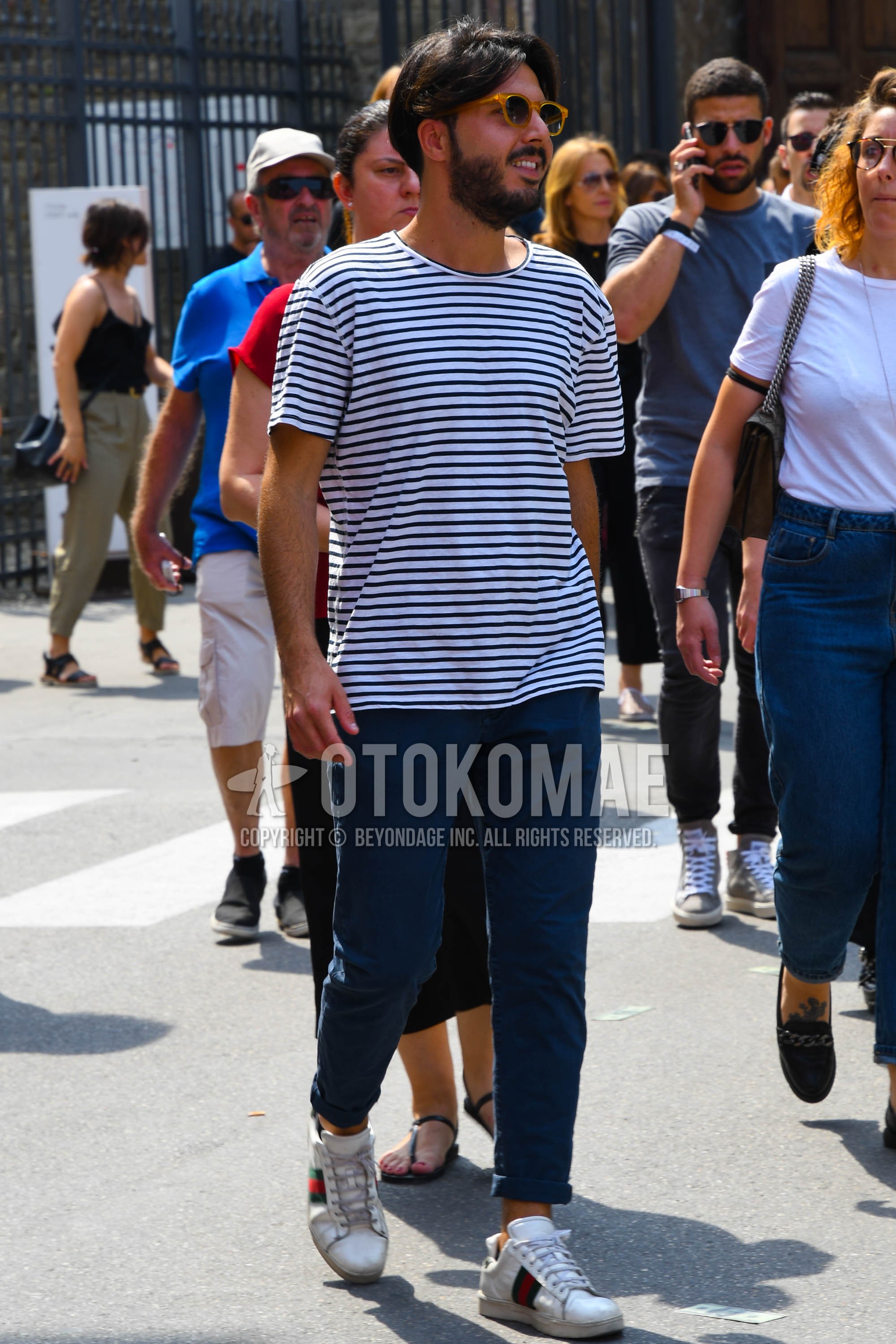 Men's spring summer outfit with beige plain sunglasses, white horizontal stripes t-shirt, navy plain chinos, white low-cut sneakers.