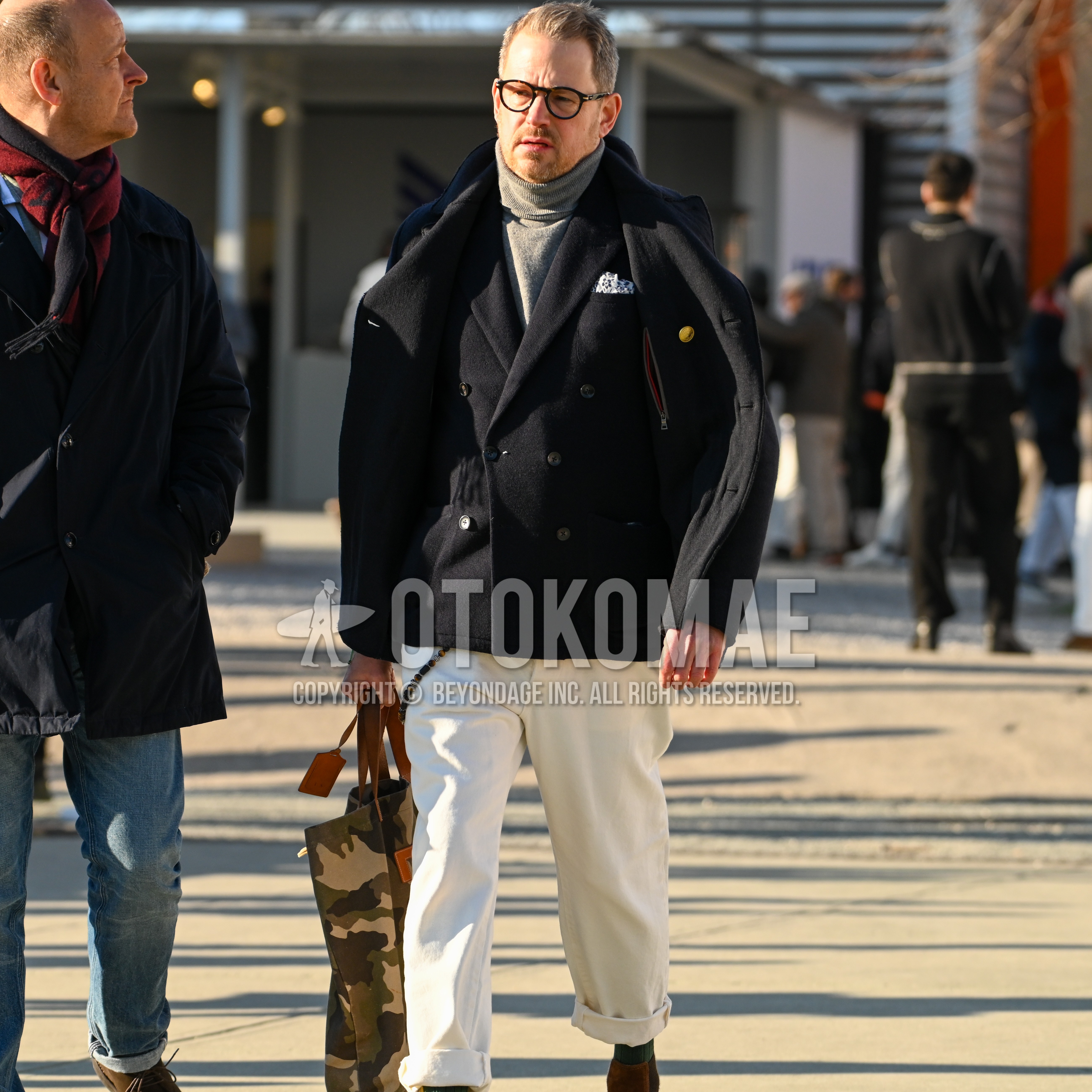 Men's autumn winter outfit with tortoiseshell glasses, black plain p coat, gray plain turtleneck knit, white plain cotton pants, camouflage tote bag.