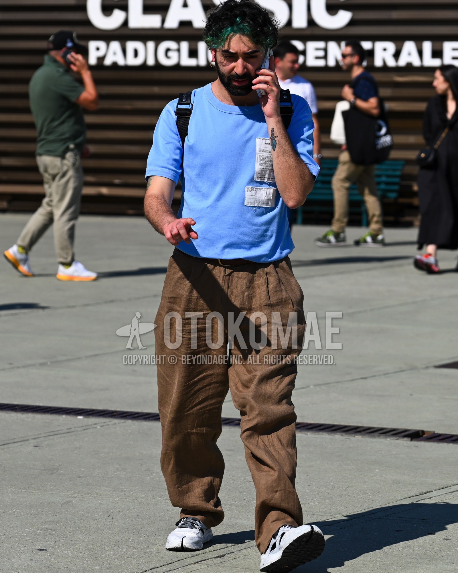 Men's spring summer outfit with light blue one point t-shirt, brown plain wide pants, brown plain pleated pants, white low-cut sneakers.
