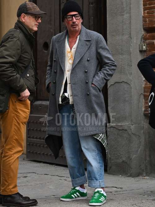 黒無地のニットキャップ、黒無地のメガネ、グレー無地のアルスターコート、白無地のフリースジャケット、黒無地のカーディガン、グリーンチェックのシャツ、白無地のTシャツ、ブルー無地のデニム/ジーンズ、白無地のソックス、アディダスのグリーンローカットのスニーカーを合わせた秋冬のメンズコーデ・着こなし。