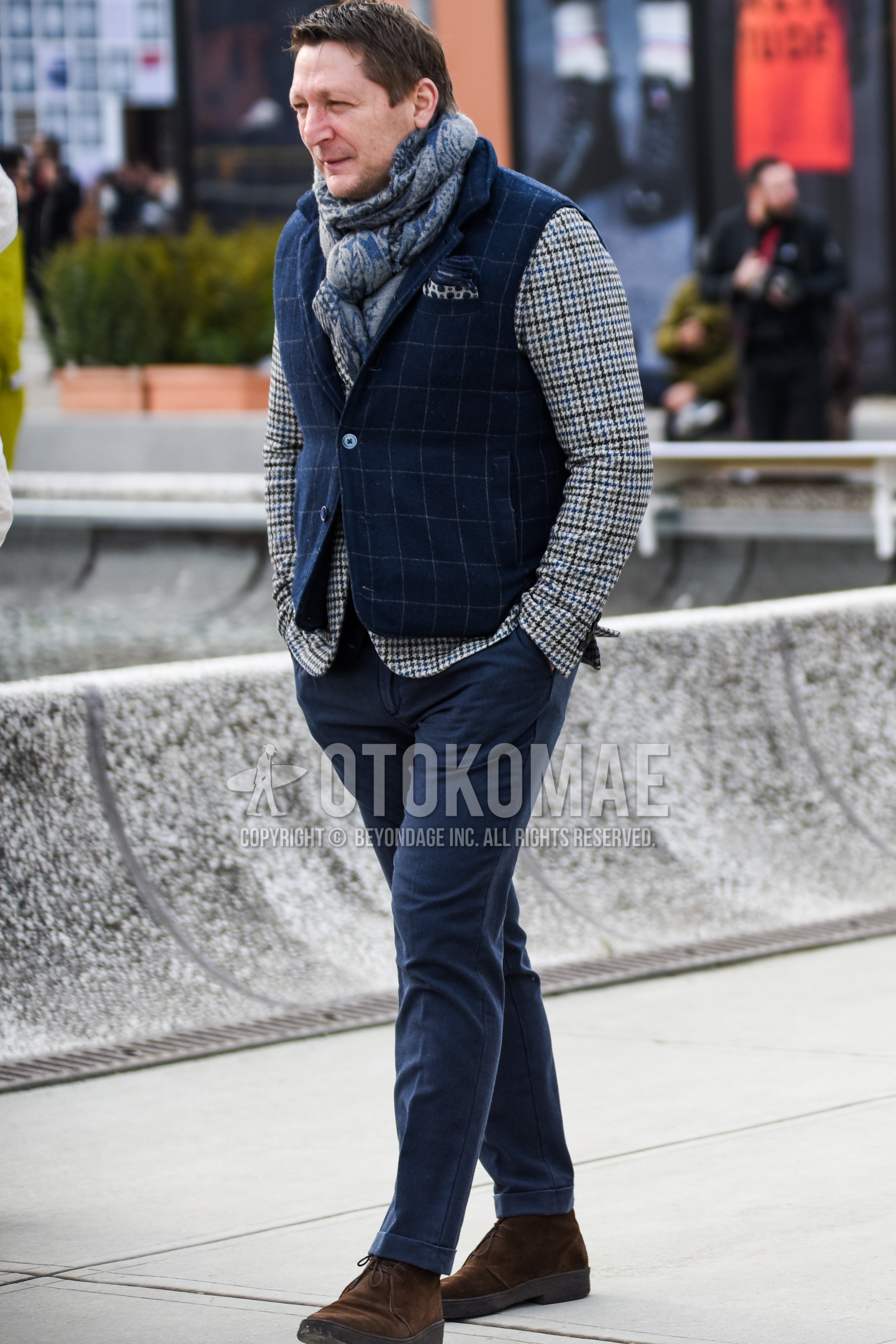 Men's autumn winter outfit with navy scarf scarf, navy check down jacket, navy check casual vest, beige check tailored jacket, navy plain chinos, brown chukka boots.