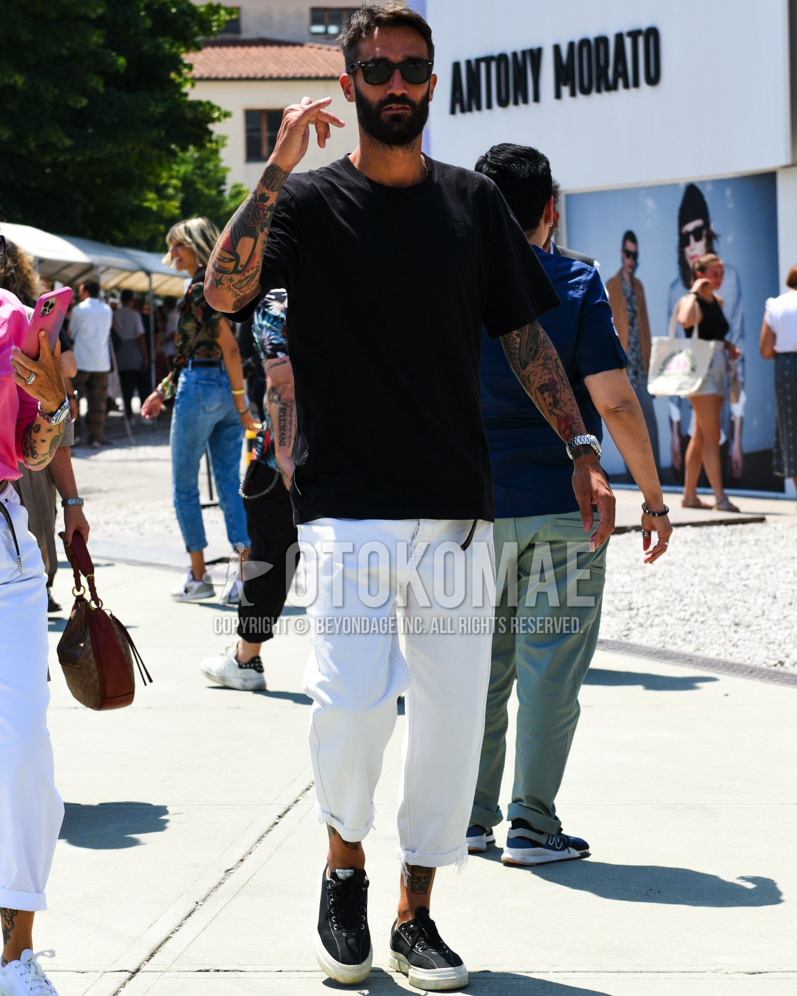 Men's spring summer outfit with black plain sunglasses, black plain t-shirt, white plain cotton pants, white plain cropped pants, black low-cut sneakers.