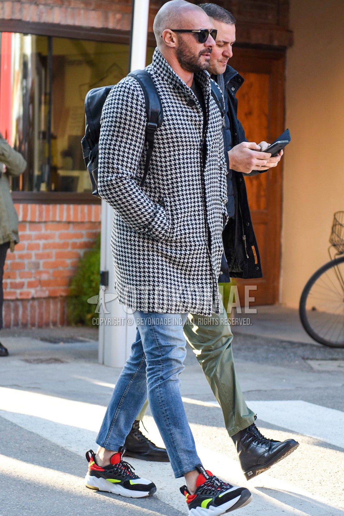 Men's autumn winter outfit with black plain sunglasses, white black check stenkarrer coat, light blue plain ankle pants, light blue plain denim/jeans, multi-color low-cut sneakers, black plain backpack.