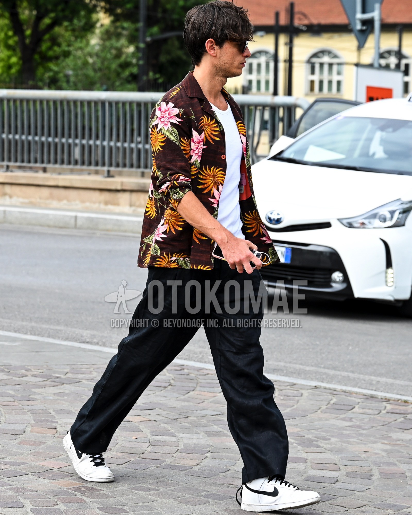 Men's spring summer outfit with brown whole pattern shirt, black plain slacks, white low-cut sneakers.