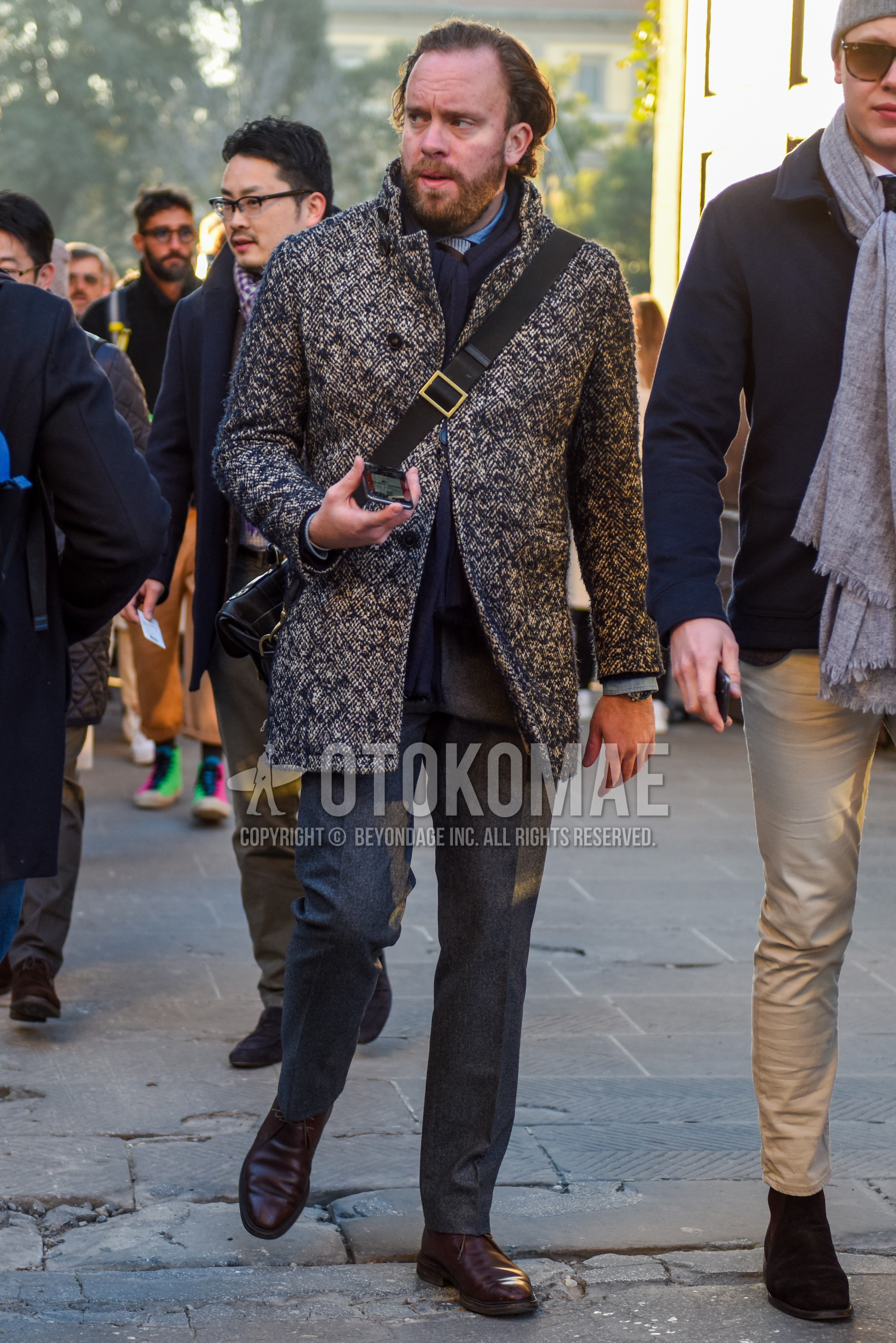 Men's autumn winter outfit with gray plain scarf, beige navy outerwear chester coat, brown chukka boots, black plain shoulder bag, gray plain suit.