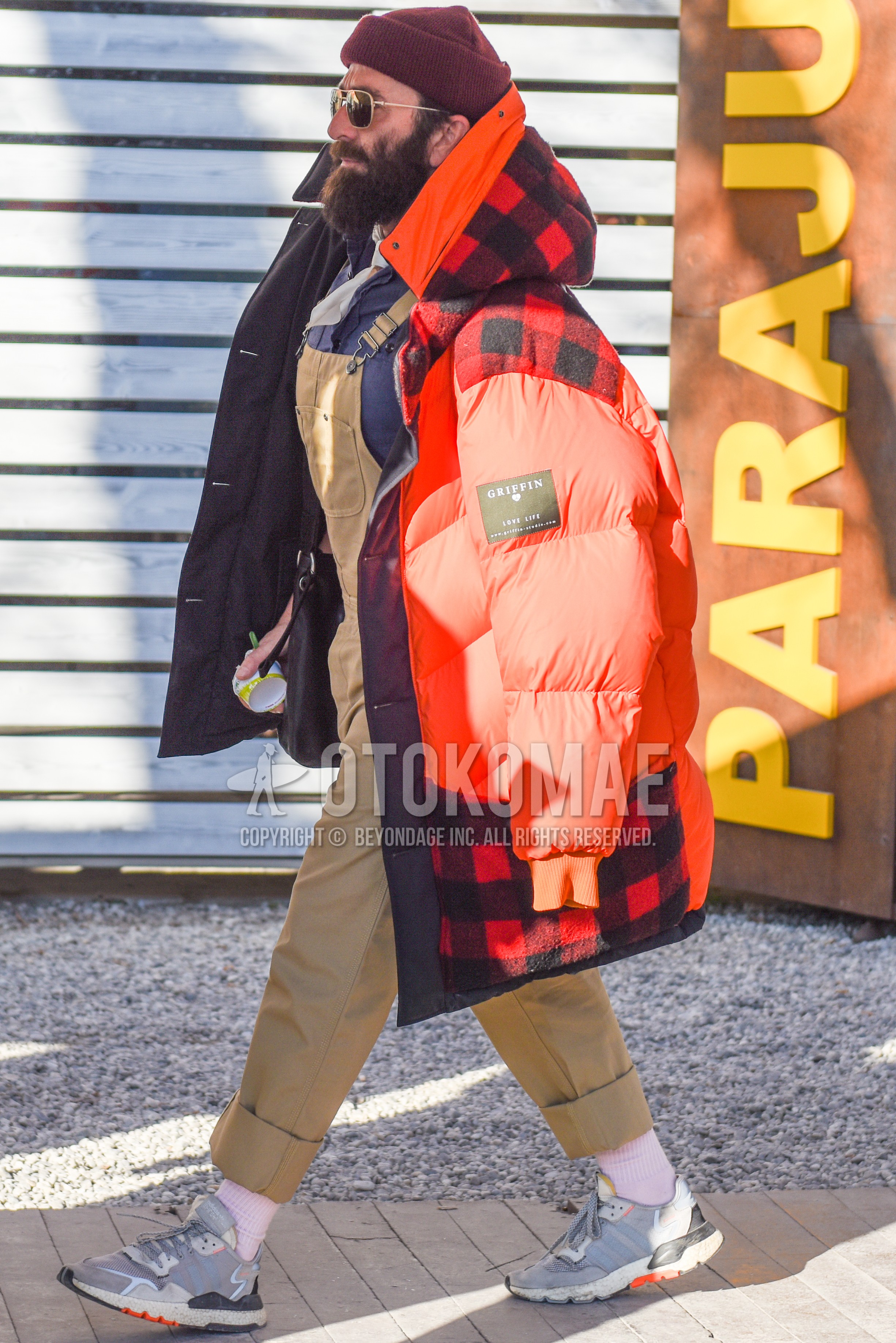 Men's autumn winter outfit with red plain knit cap, gold plain sunglasses, white plain bandana/neckerchief, orange red plain down jacket, beige plain jumpsuit, gray plain shirt, white plain socks, gray low-cut sneakers.