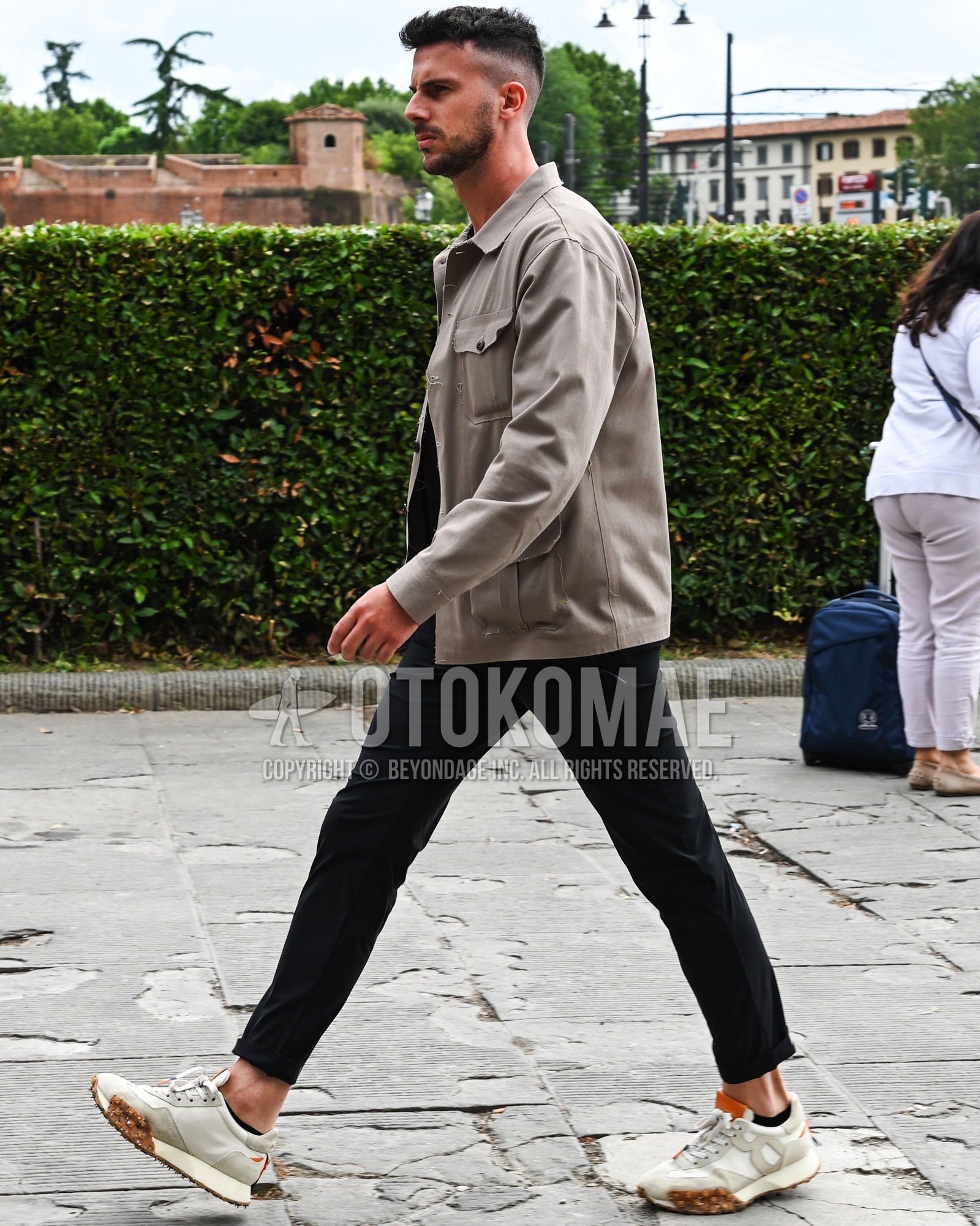 Men's spring summer autumn outfit with beige plain coverall, black plain chinos, black plain socks, white low-cut sneakers.