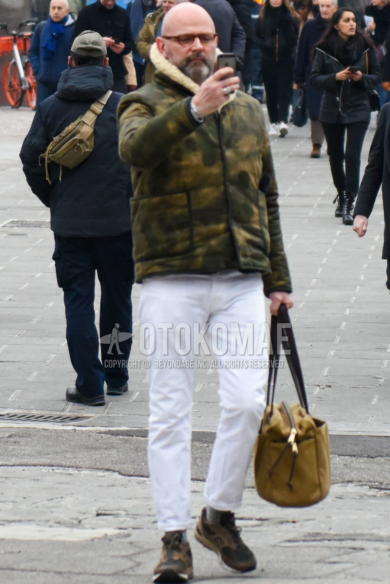 Men's winter outfit with plain glasses, multi-color outerwear, white plain denim/jeans, brown low-cut sneakers, beige plain boston bag.