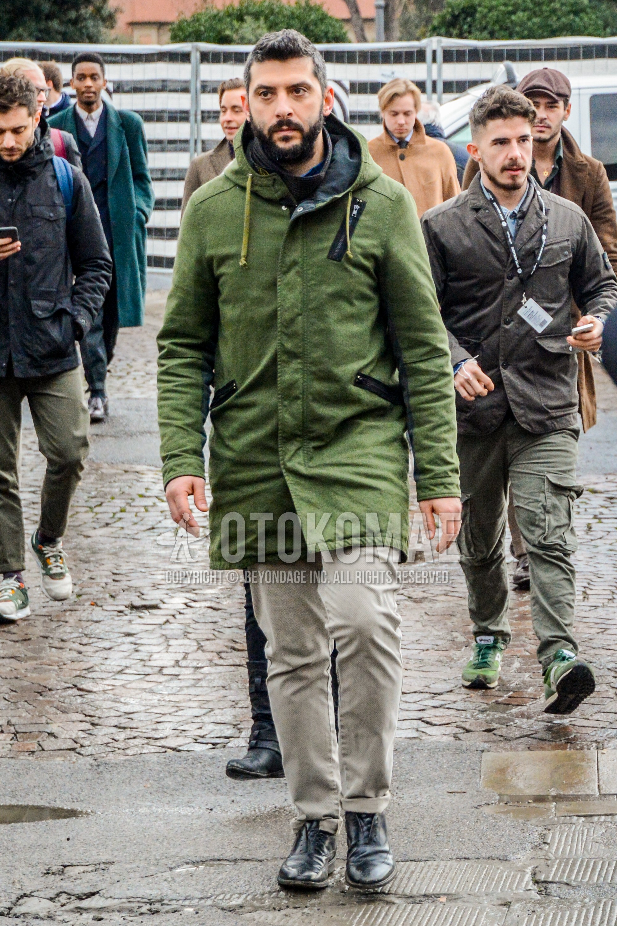 Men's autumn winter outfit with olive green plain hooded coat, beige plain chinos, black wing-tip shoes leather shoes.