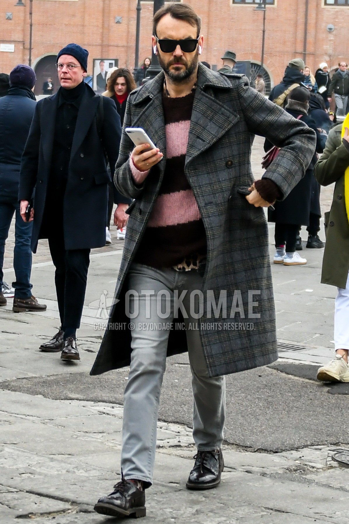 Men's autumn winter outfit with black plain sunglasses, gray check trench coat, pink brown horizontal stripes sweater, gray plain denim/jeans, brown wing-tip shoes leather shoes.