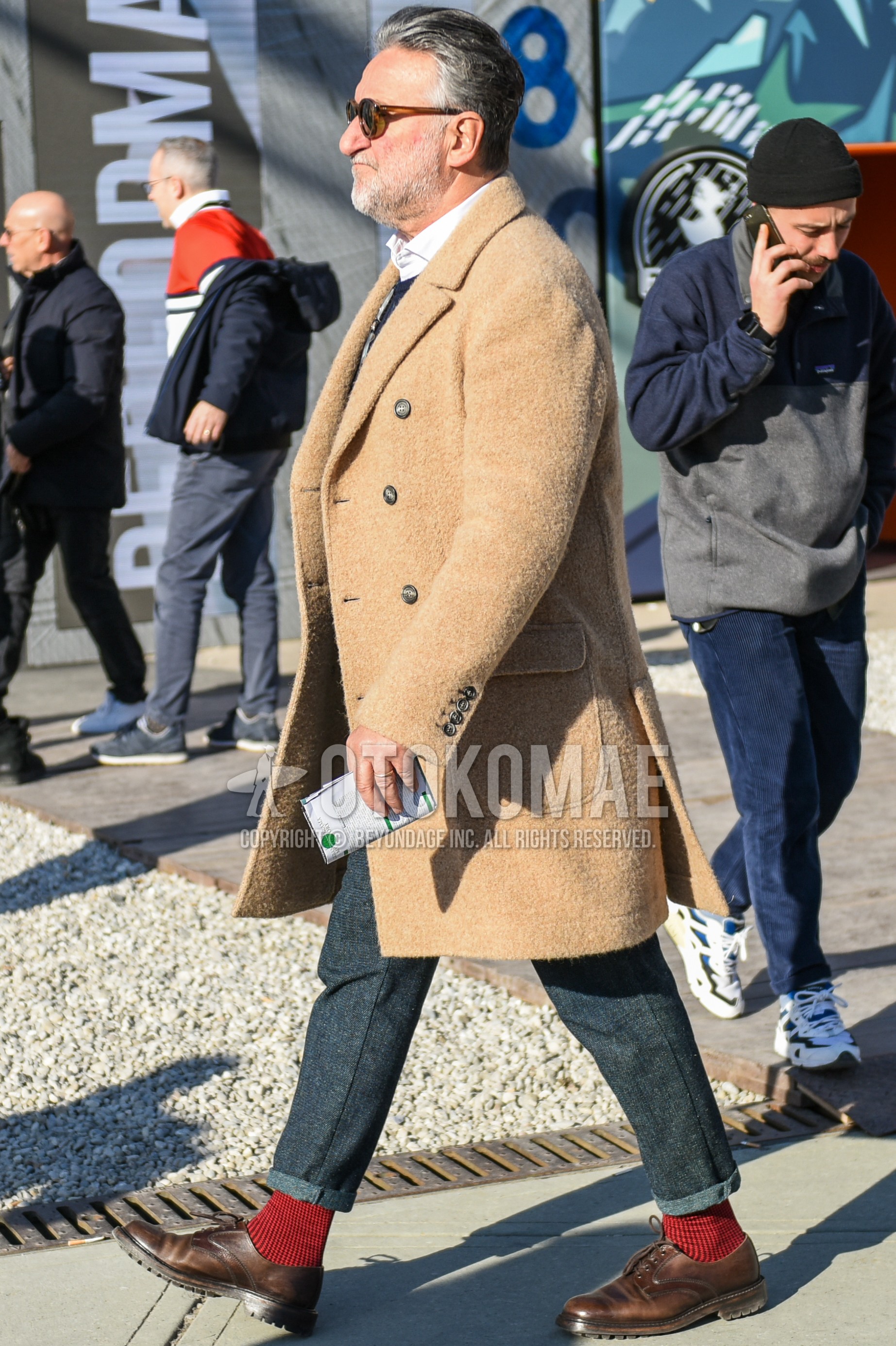 Men's autumn winter outfit with brown tortoiseshell sunglasses, beige plain chester coat, white plain shirt, gray plain slacks, red check socks, brown plain toe leather shoes.
