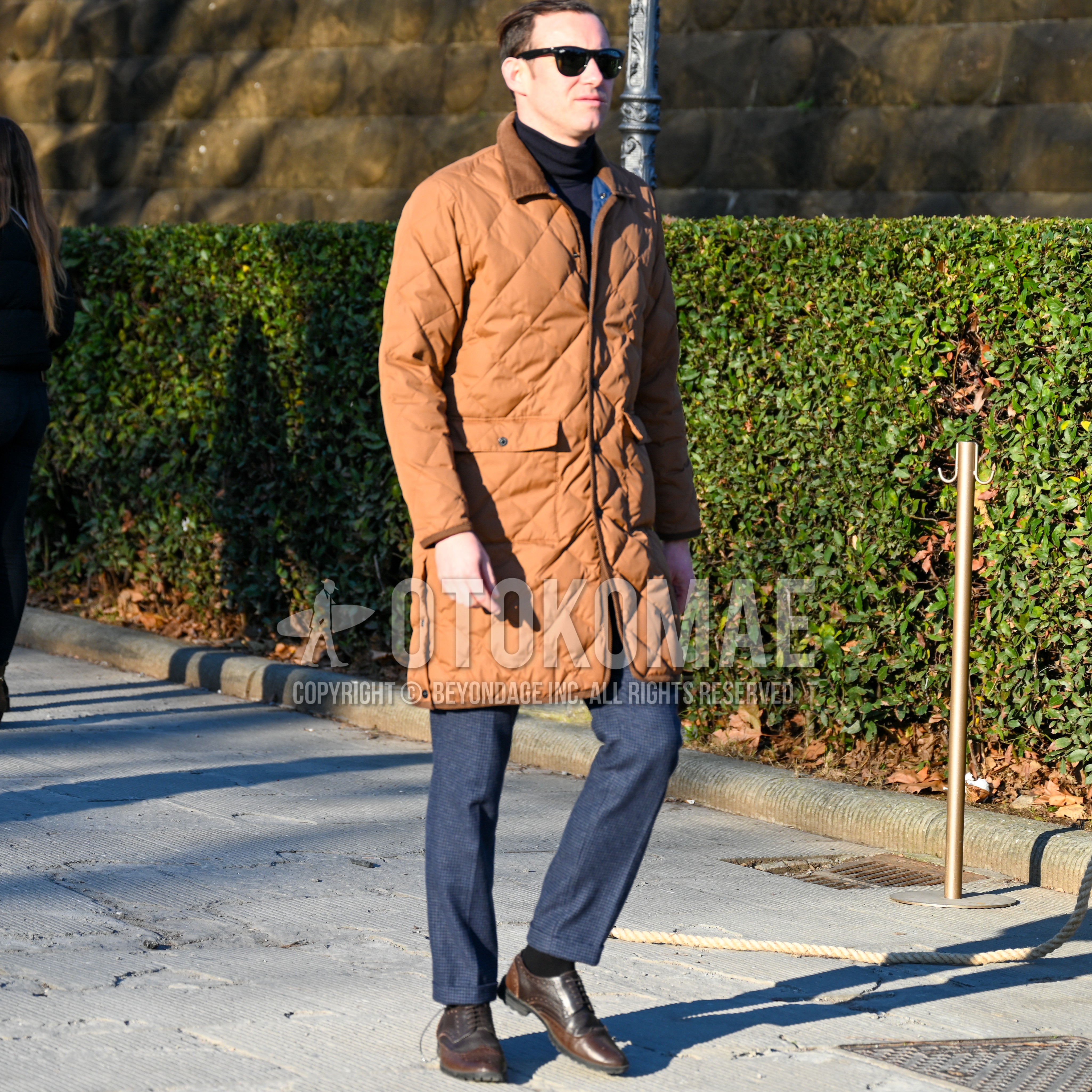 Men's autumn winter outfit with black plain sunglasses, brown beige plain quilted jacket, black plain turtleneck knit, navy check slacks, black plain socks, brown wing-tip shoes leather shoes.