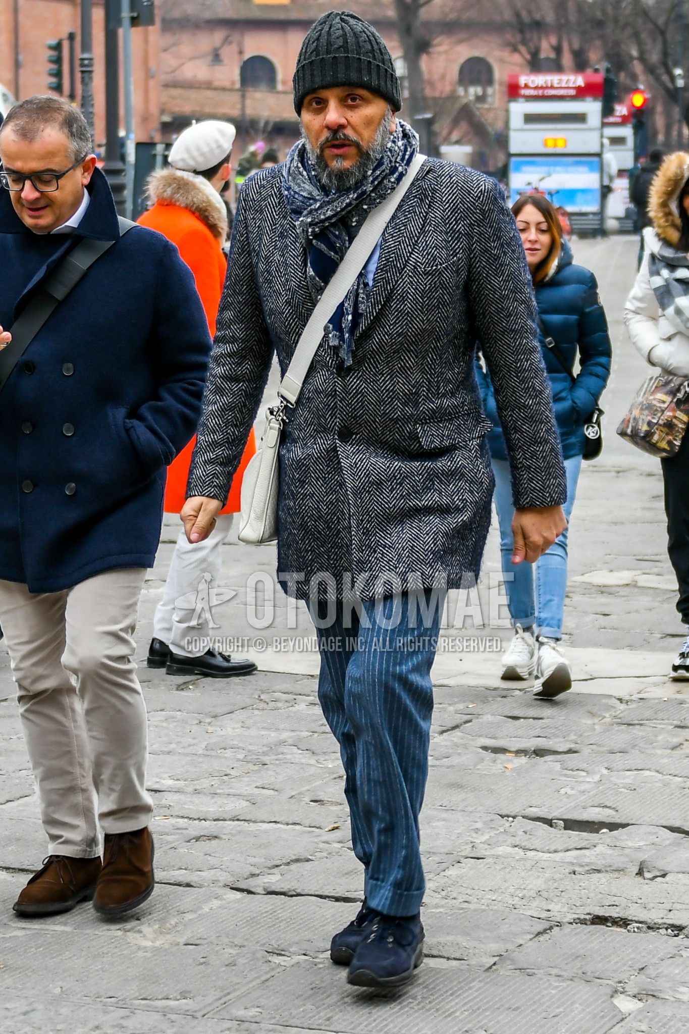 Men's autumn winter outfit with gray plain knit cap, gray scarf scarf, gray herringbone chester coat, gray stripes slacks, navy low-cut sneakers, white plain shoulder bag.