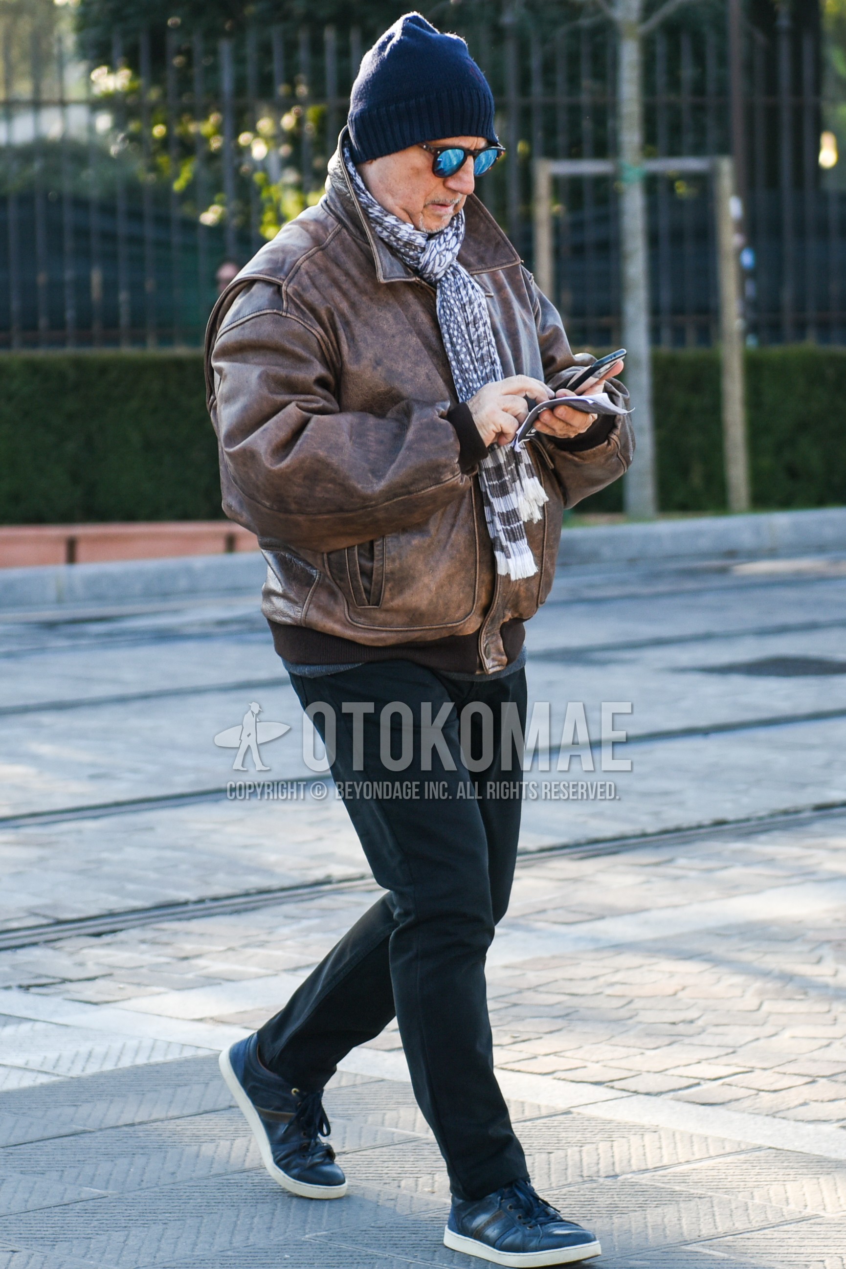 Men's autumn winter outfit with gray plain knit cap, brown tortoiseshell sunglasses, gray scarf scarf, brown plain leather jacket, brown plain military jacket, black plain cotton pants, gray low-cut sneakers.