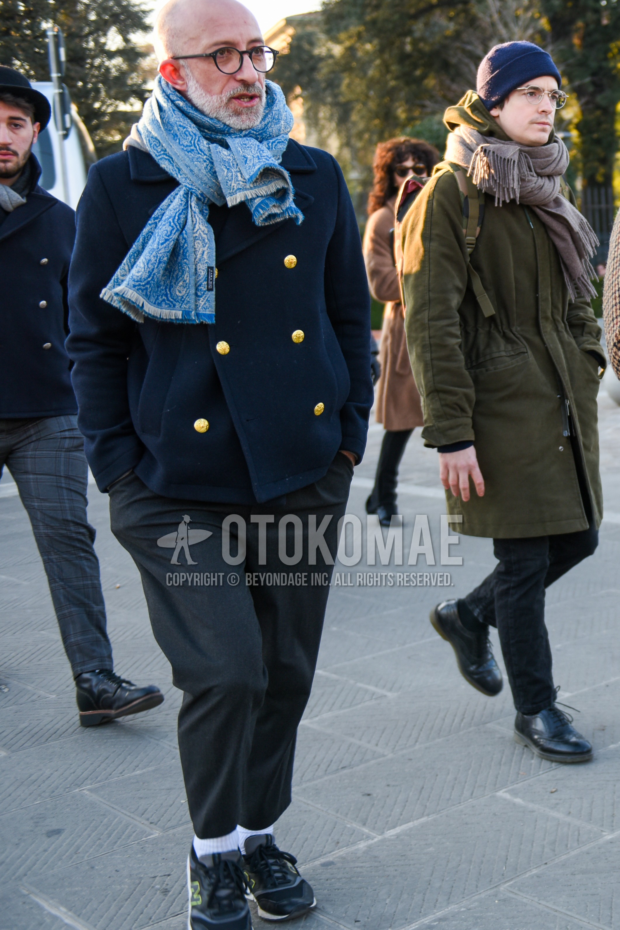 Men's autumn winter outfit with black plain glasses, light blue scarf scarf, navy plain p coat, gray plain slacks, gray plain cropped pants, white plain socks, gray low-cut sneakers.