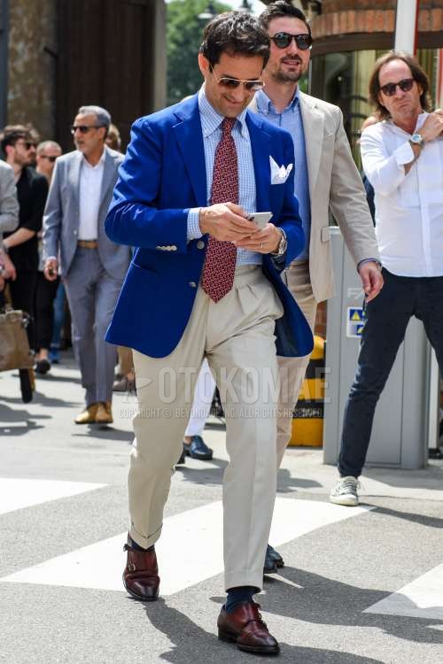 ゴールド・ブラウン無地のサングラス、ブルー無地のテーラードジャケット、水色チェックのシャツ、ベージュ・白無地のコットンパンツ、ネイビー無地のソックス、ブラウンモンクシューズの革靴、レッドネクタイのネクタイを合わせた春夏秋のメンズコーデ・着こなし。