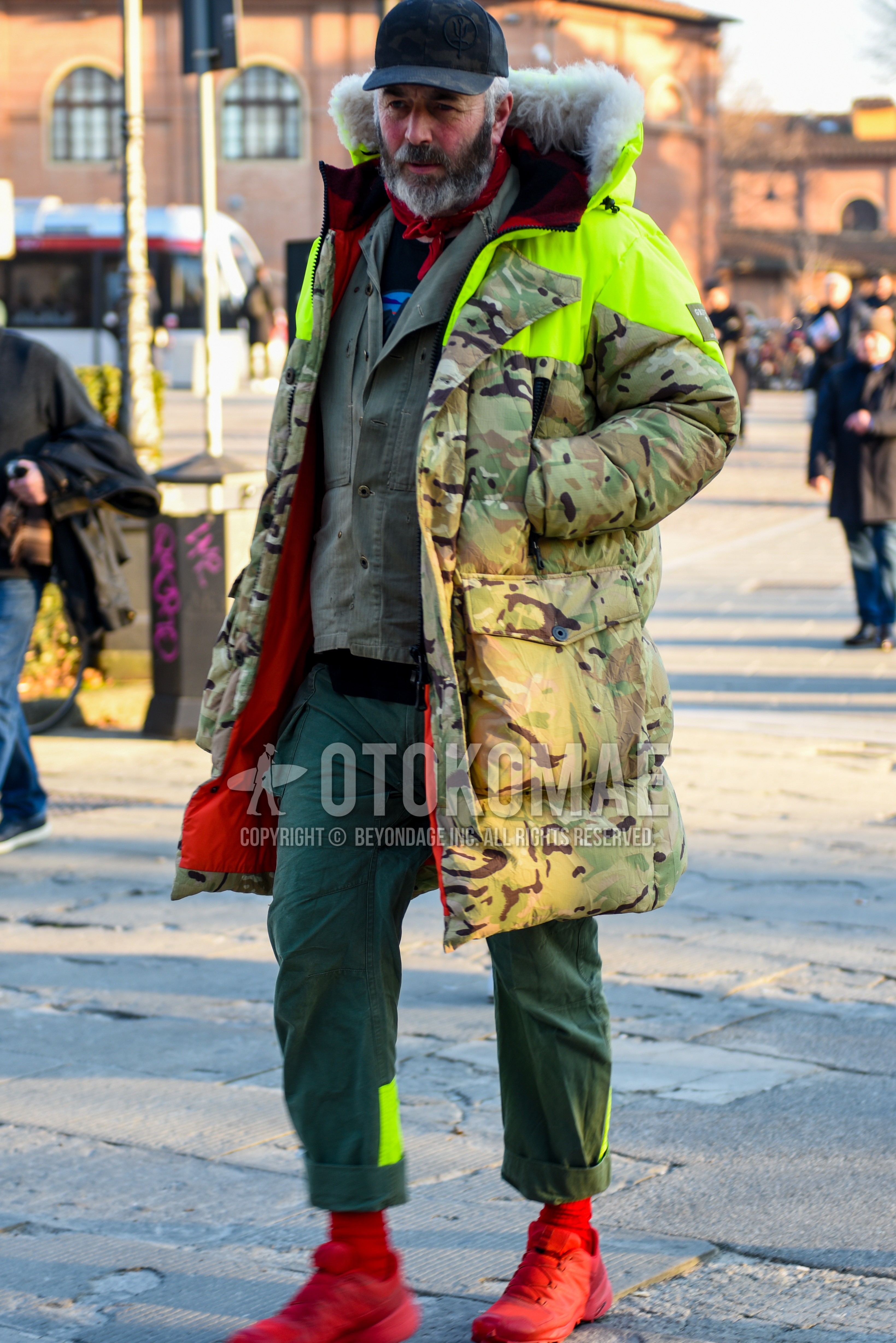 Men's autumn winter outfit with black plain baseball cap, green camouflage down jacket, olive green plain shirt jacket, black graphic sweater, olive green plain cargo pants, red plain socks, red high-cut sneakers.