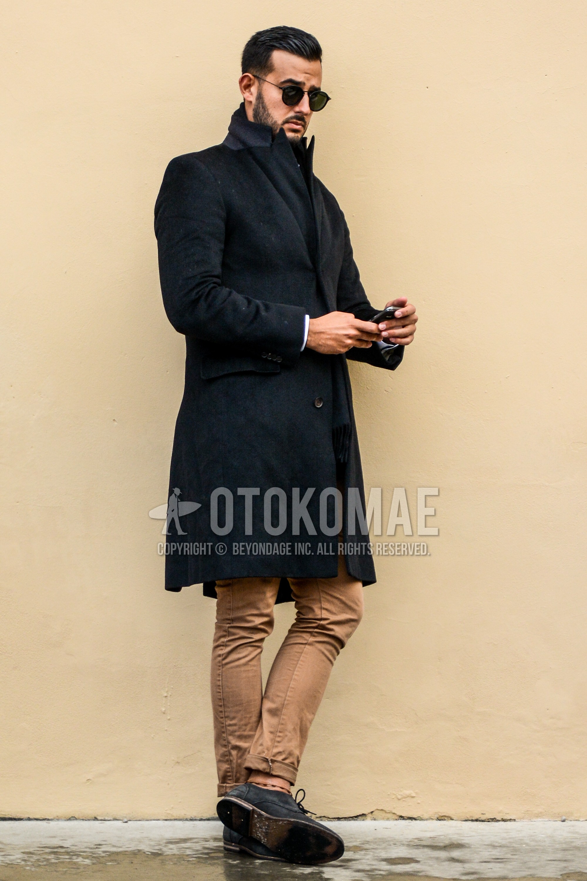 Men's autumn winter outfit with plain sunglasses, black plain chester coat, beige plain chinos, black suede shoes leather shoes, wing-tip shoes leather shoes.