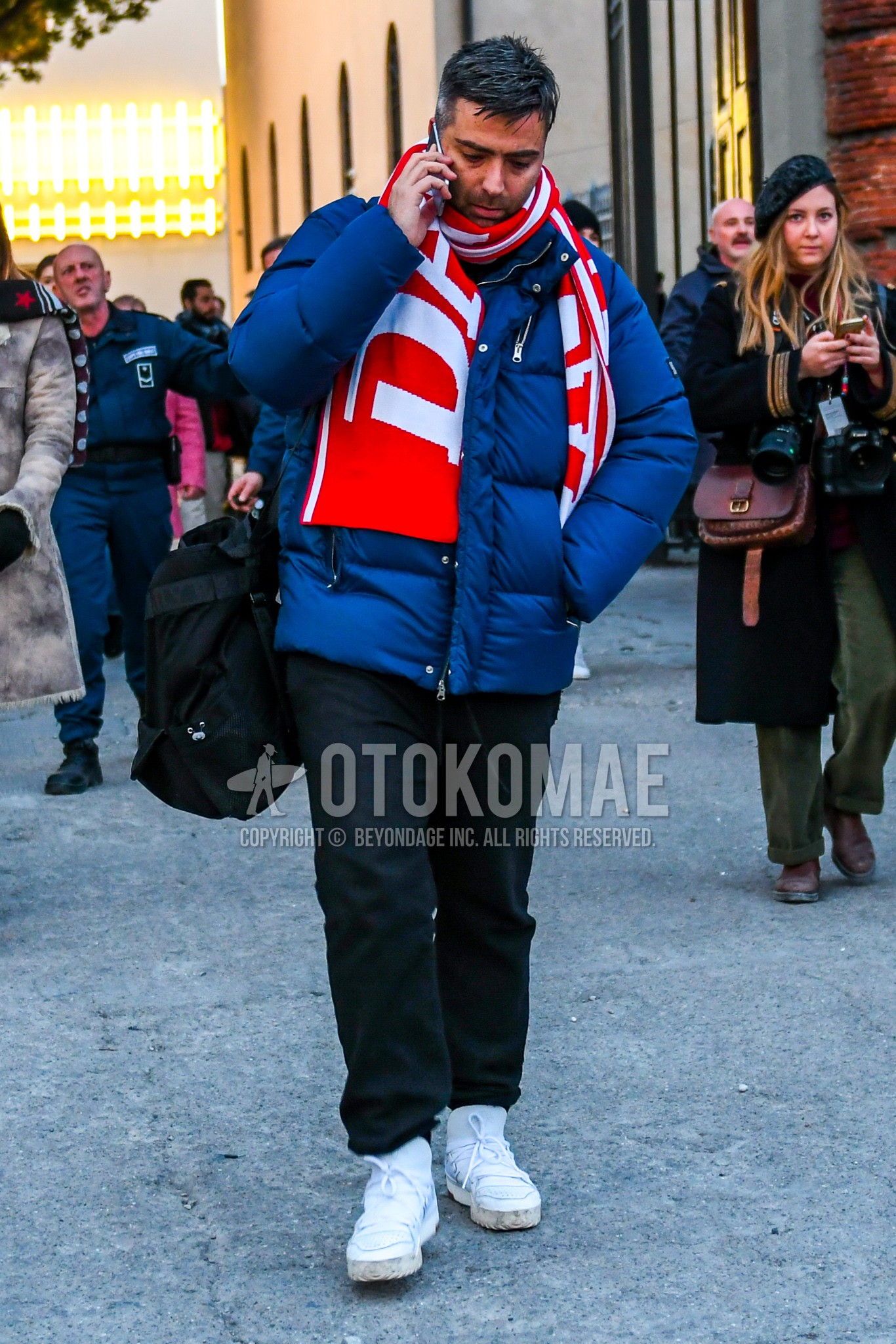 Men's winter outfit with red graphic scarf, blue plain down jacket, black plain easy pants, white sneakers.