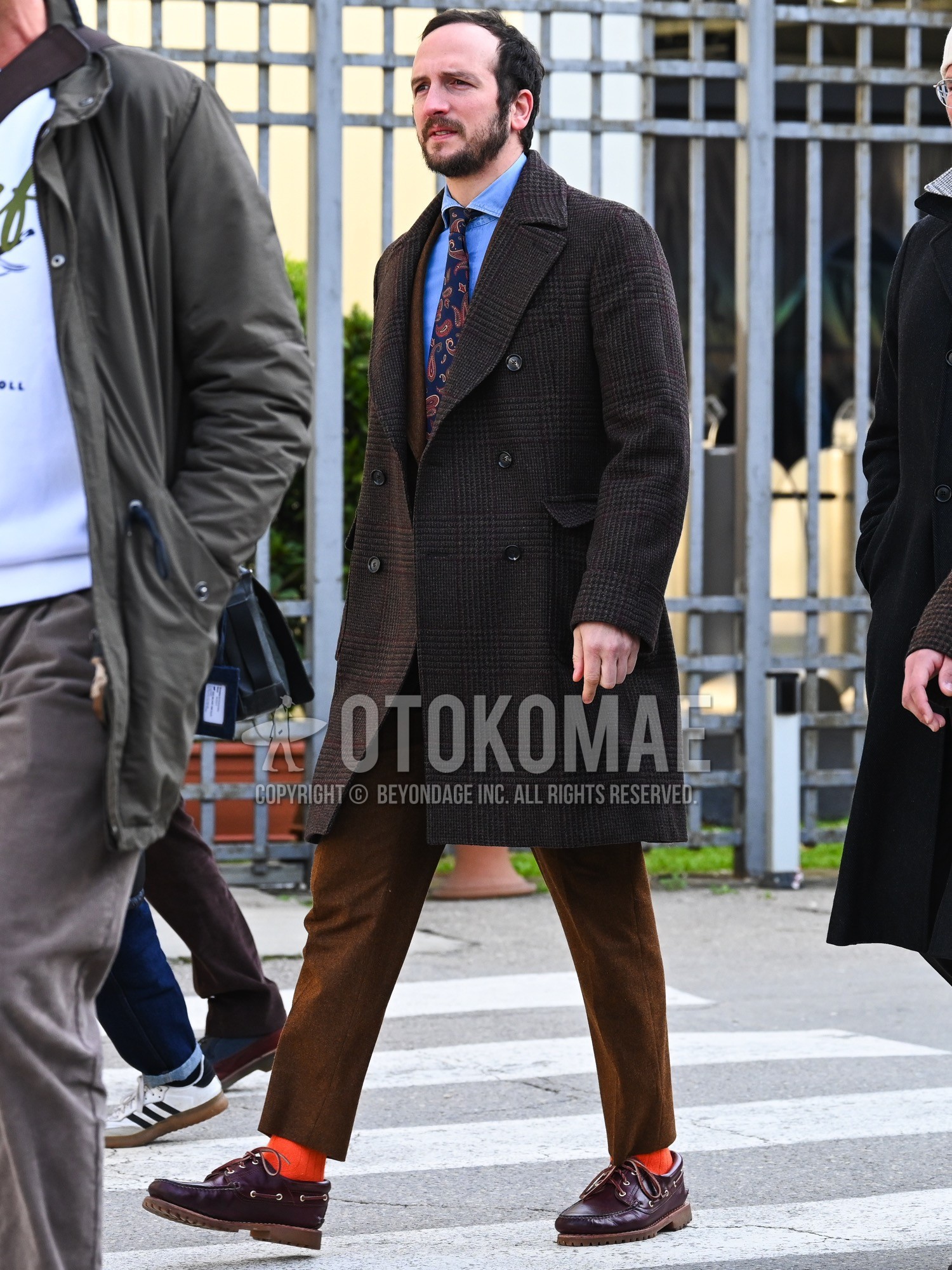 Men's autumn winter outfit with brown check ulster coat, orange plain socks, brown moccasins/deck shoes leather shoes, brown plain suit, blue graphic necktie.