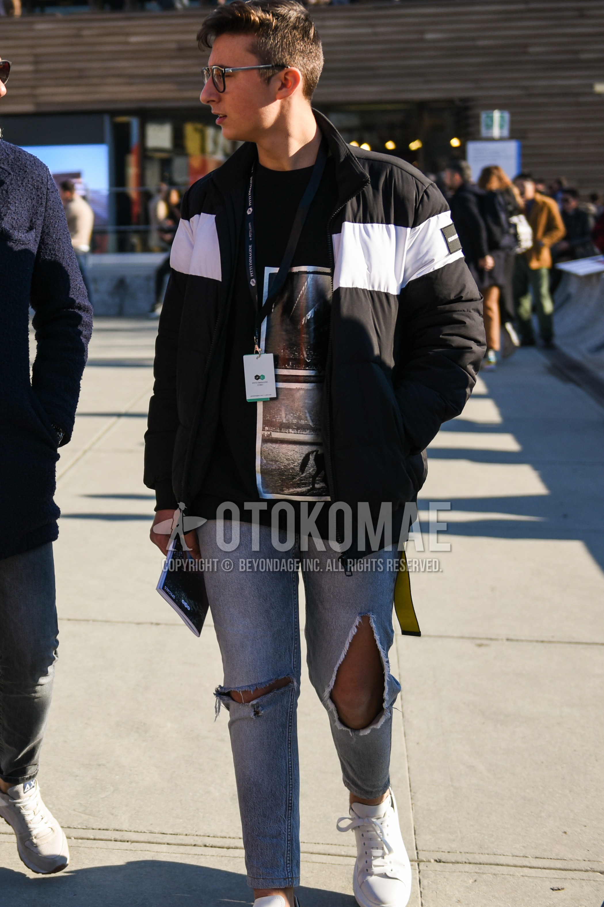 Men's autumn winter outfit with black plain sunglasses, black plain down jacket, black graphic sweatshirt, gray plain damaged jeans, white low-cut sneakers.