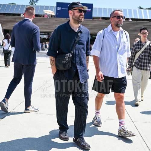 黒レタードのベースボールキャップ、黒無地のサングラス、ネイビー無地のシャツ、ネイビーストライプのスラックス、キーン　ユニークのネイビーサンダル、アークテリクスの黒無地のショルダーバッグを合わせた夏春のメンズコーデ・着こなし。