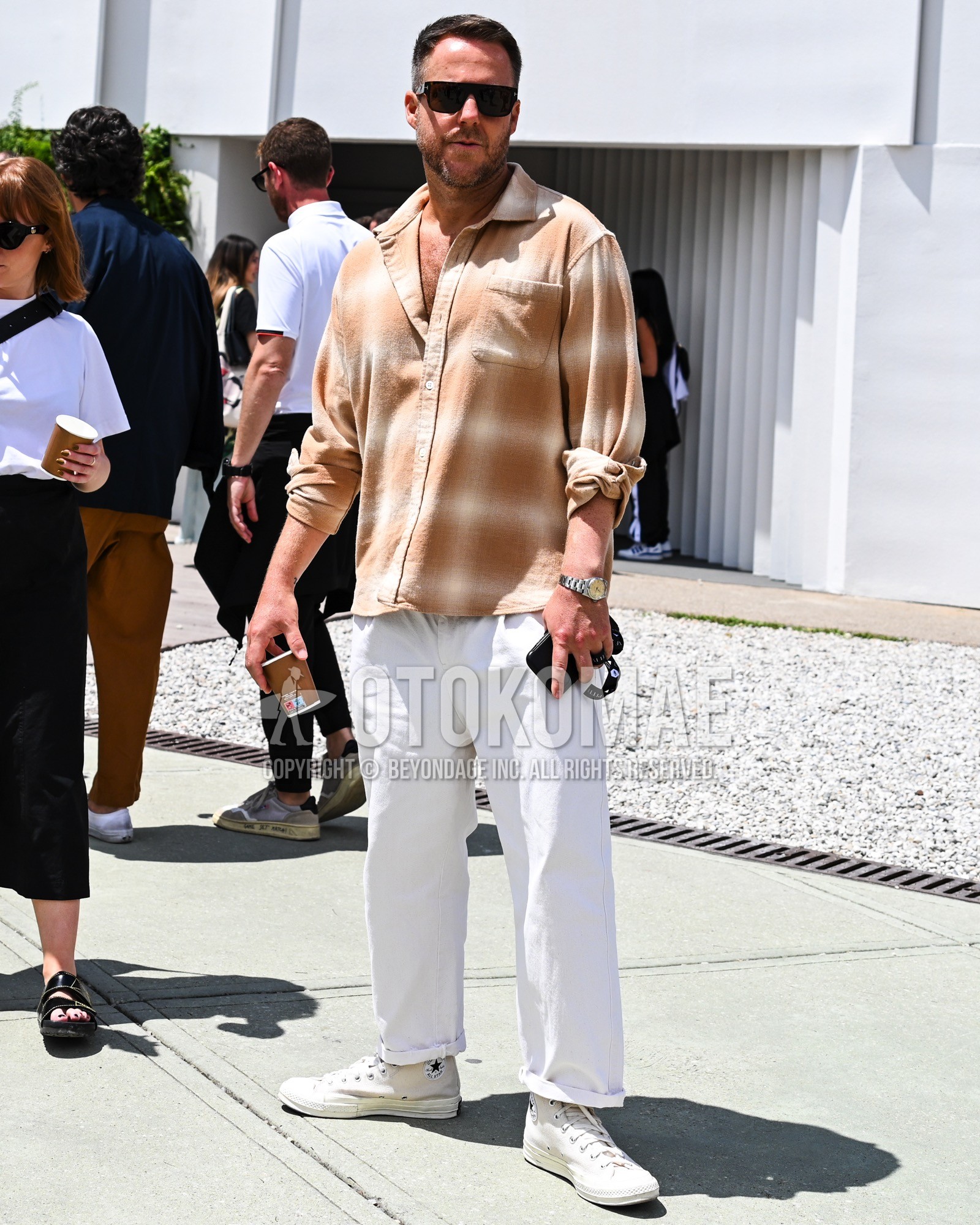 Men's spring summer outfit with black plain sunglasses, beige check shirt, white plain chinos, white low-cut sneakers.