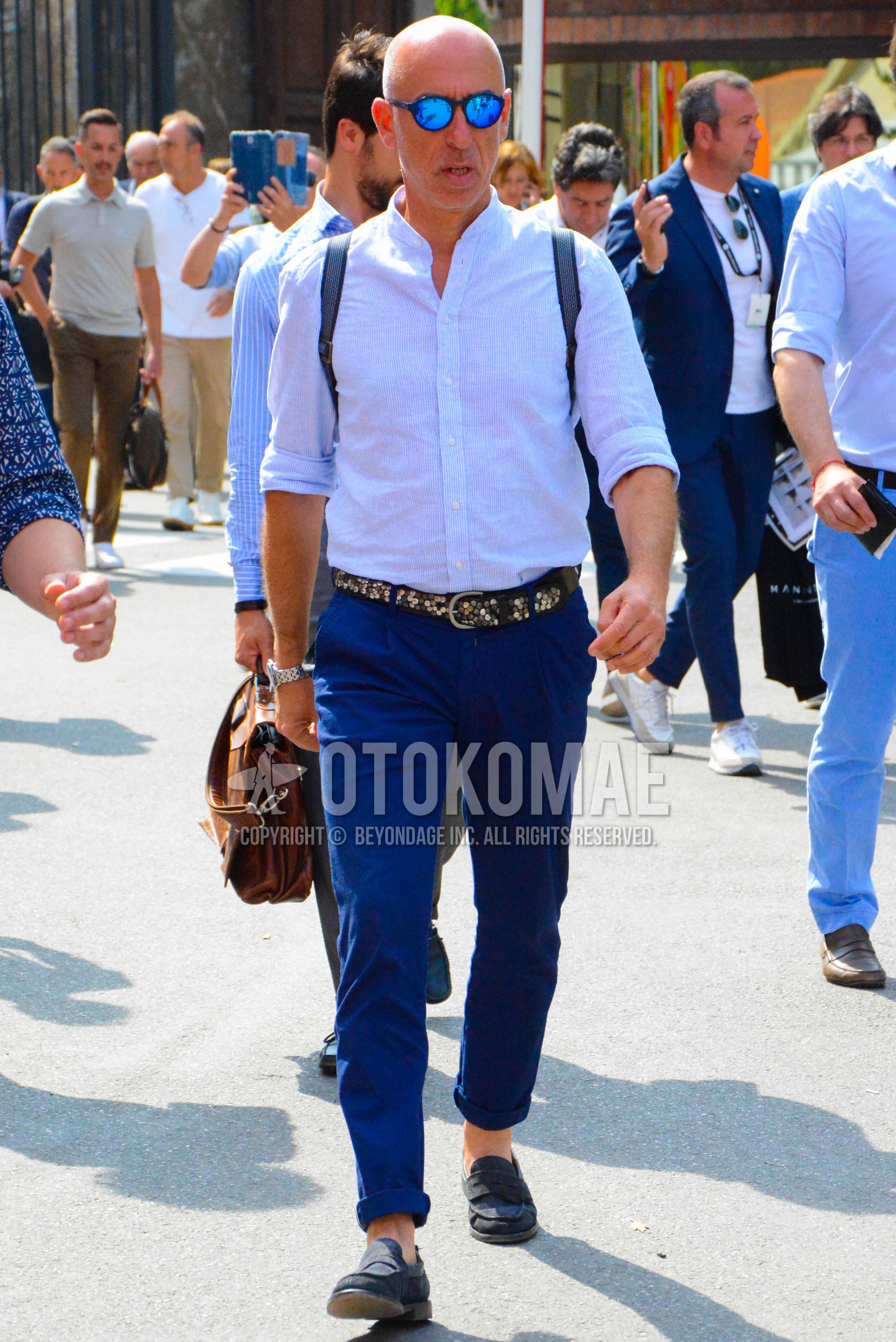 Men's spring summer outfit with black plain sunglasses, light blue stripes shirt, brown plain leather belt, navy plain chinos, navy plain pleated pants, navy coin loafers leather shoes.