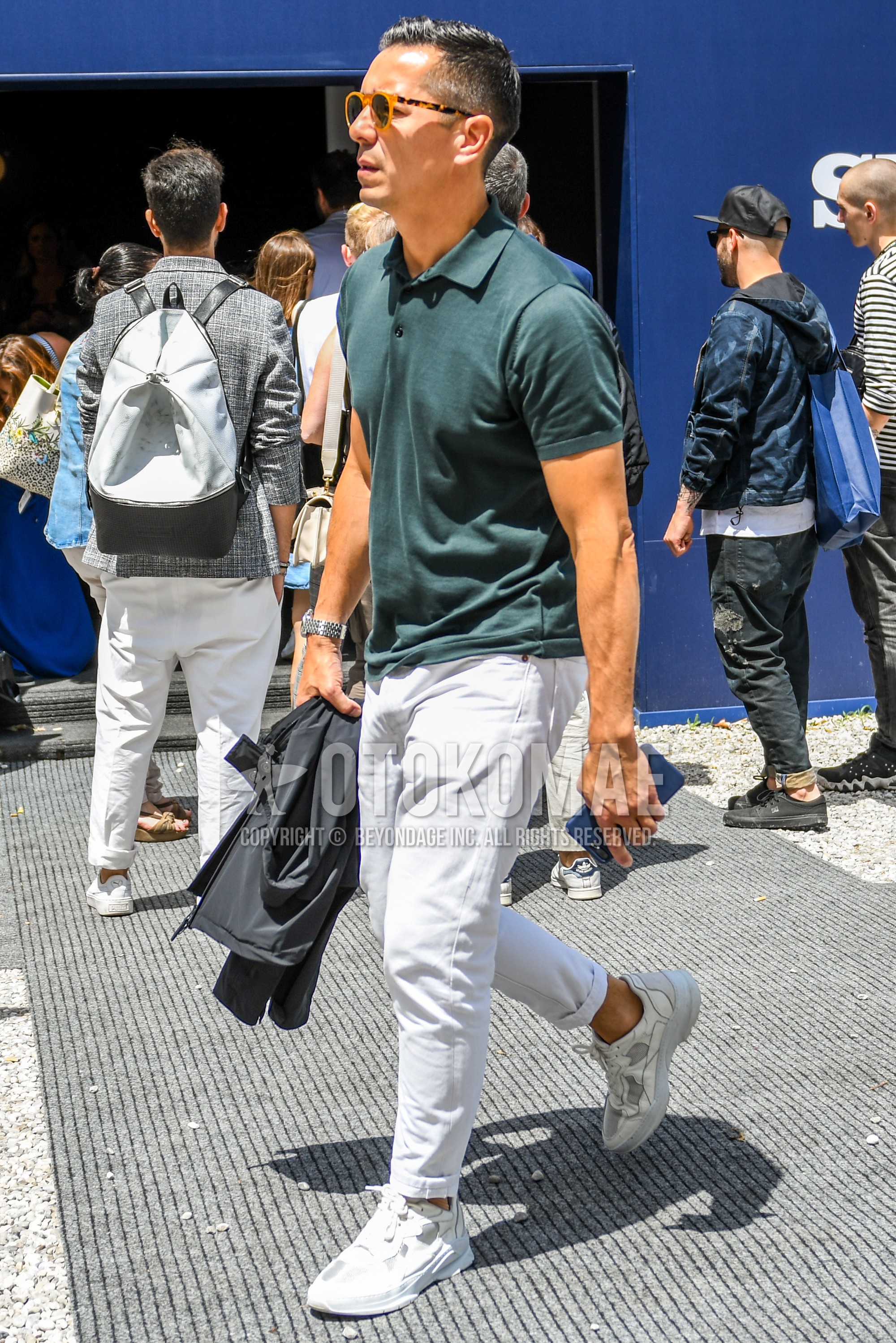 Men's spring summer outfit with brown tortoiseshell sunglasses, green plain polo shirt, white plain cotton pants, white low-cut sneakers.