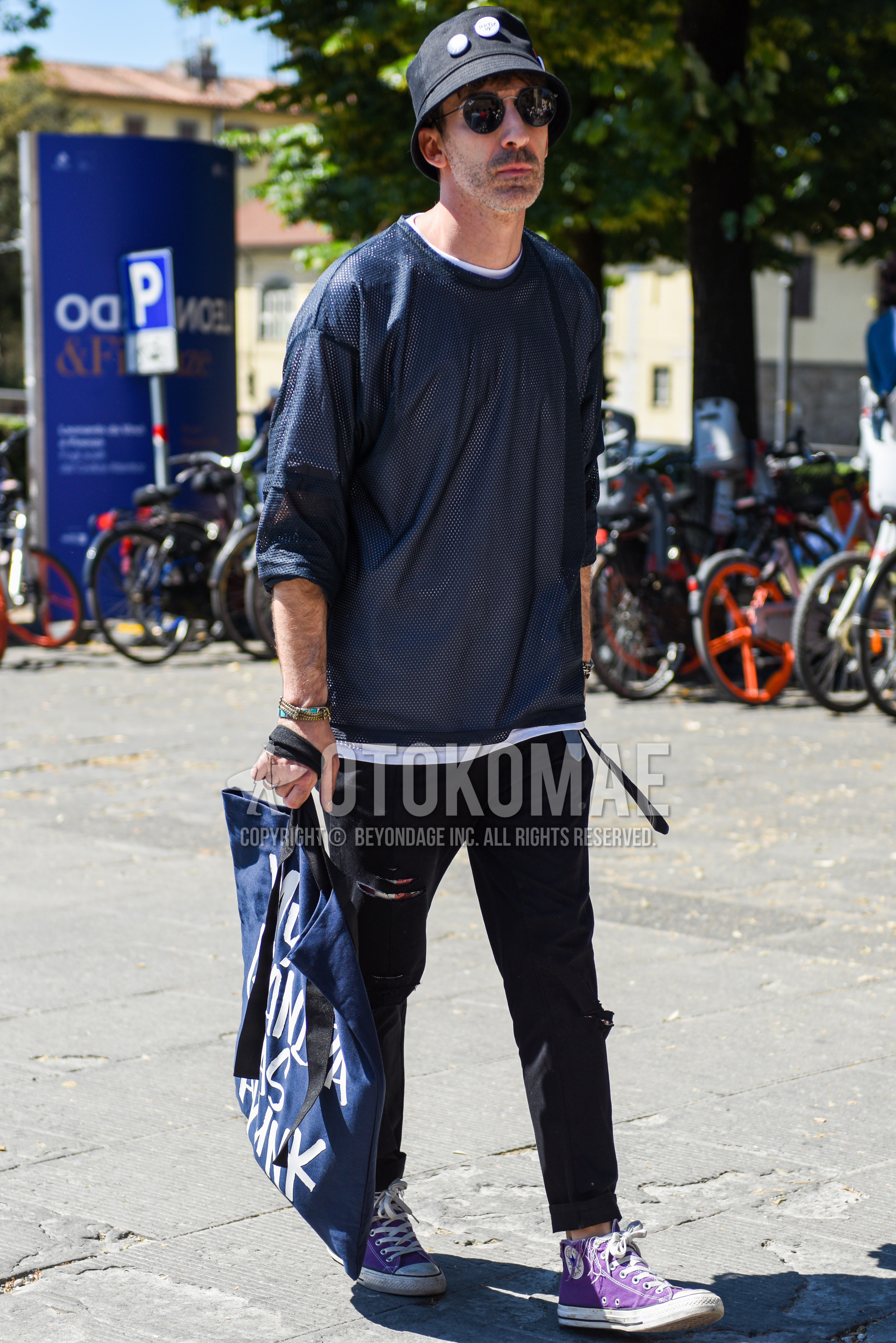 Men's spring summer outfit with black plain hat, black plain sunglasses, black plain t-shirt, white plain t-shirt, black plain damaged jeans, purple high-cut sneakers, navy graphic tote bag.