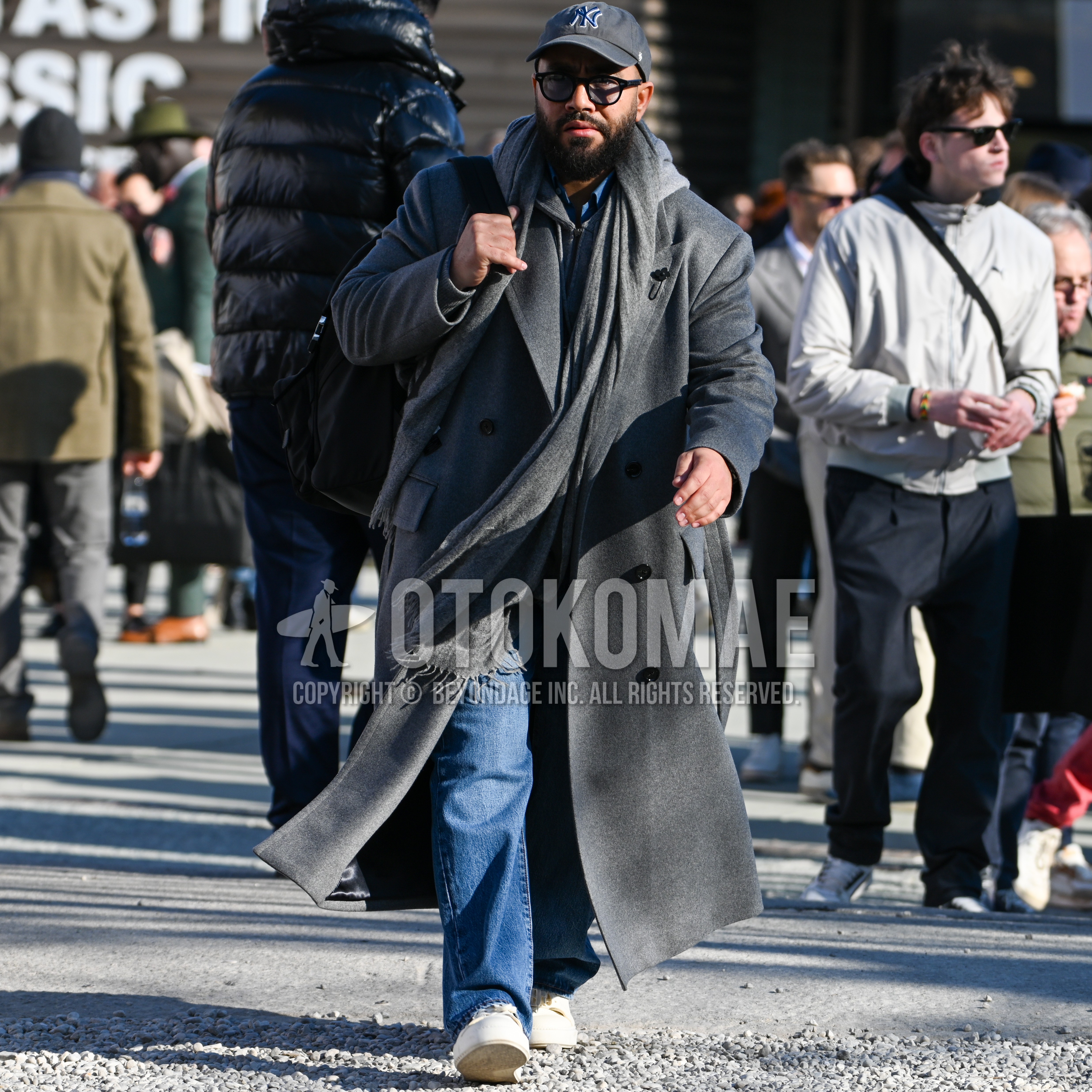 Men's autumn winter outfit with gray one point baseball cap, black plain sunglasses, gray plain scarf, gray plain chester coat, bottoms denim/jeans, white low-cut sneakers, plain backpack.