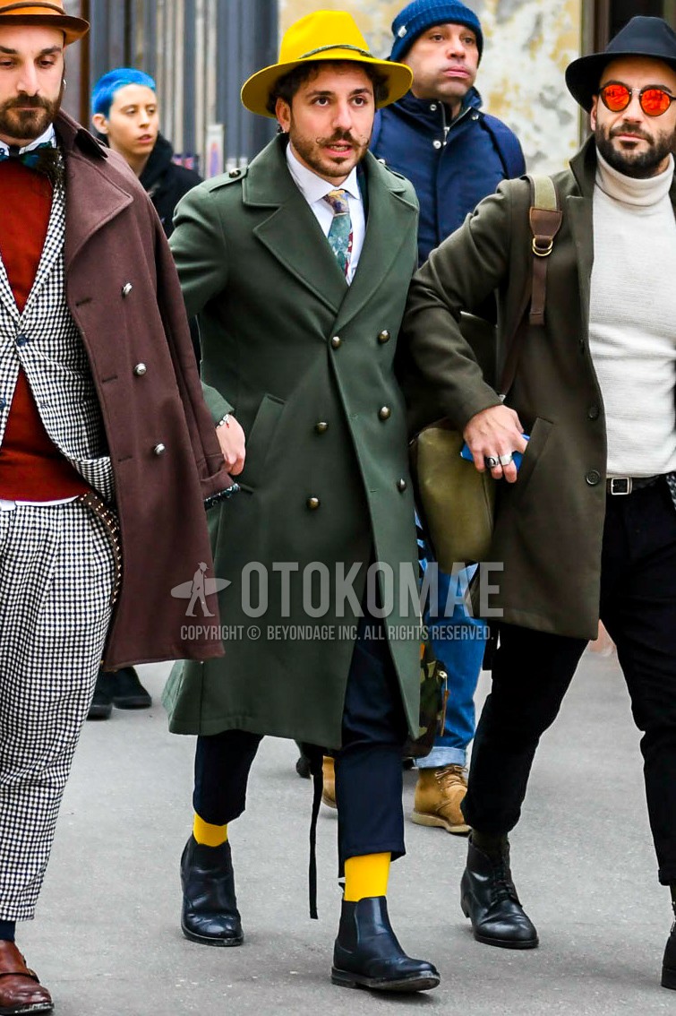 Men's autumn winter outfit with yellow plain hat, olive green plain trench coat, white plain shirt, dark gray plain slacks, yellow plain socks, black side-gore boots, multi-color necktie necktie.