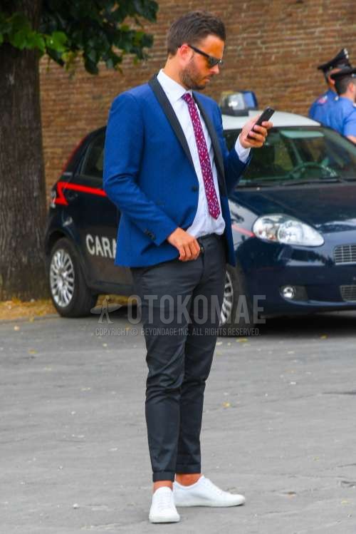 黒無地のサングラス、ネイビー無地のテーラードジャケット、白無地のシャツ、グレー無地のスラックス、白ローカットのスニーカー、レッドネクタイのネクタイを合わせた春秋のメンズコーデ・着こなし。