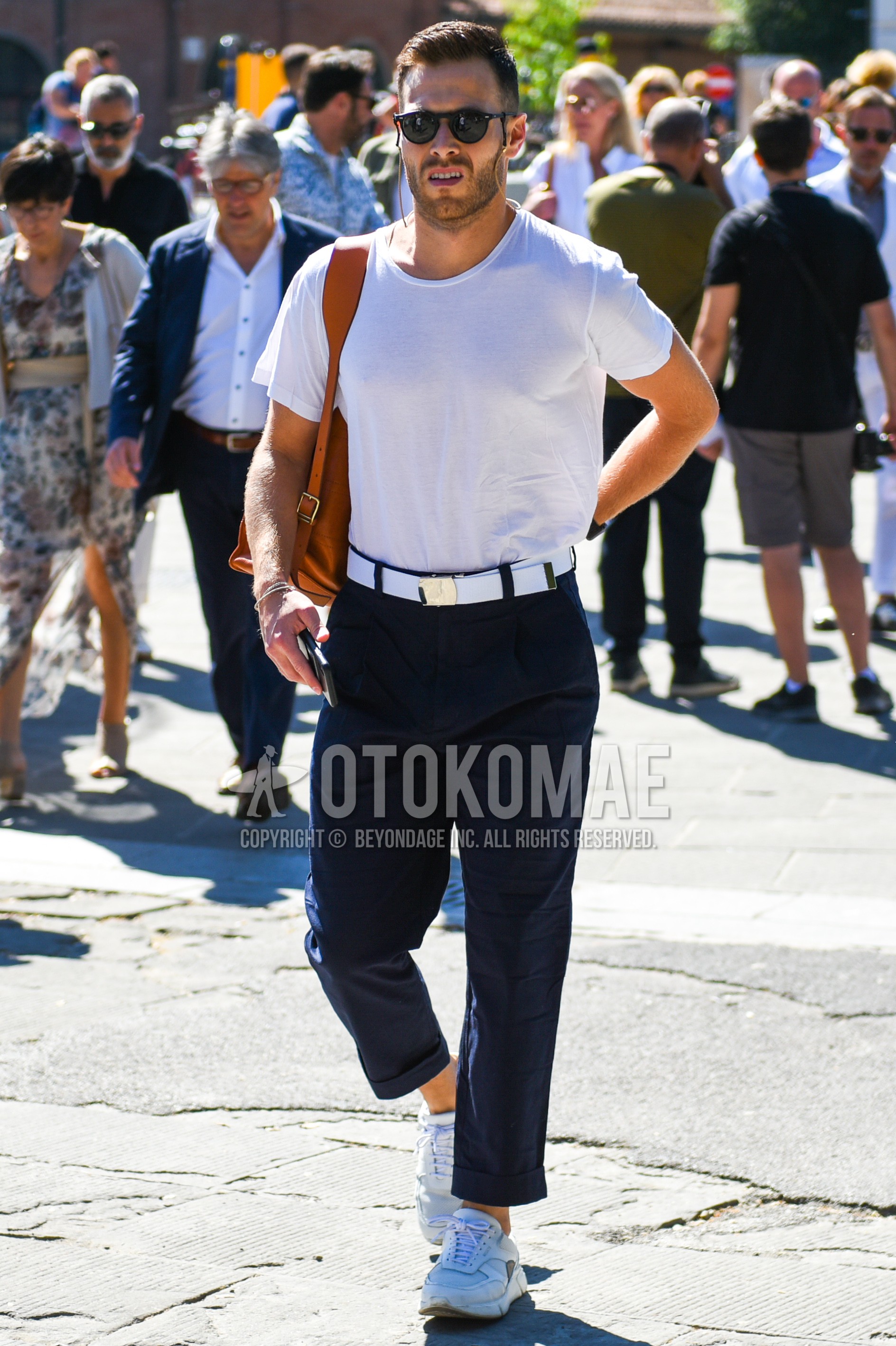 Men's summer outfit with black plain sunglasses, white plain t-shirt, white plain tape belt, dark gray plain slacks, white low-cut sneakers, brown plain shoulder bag.