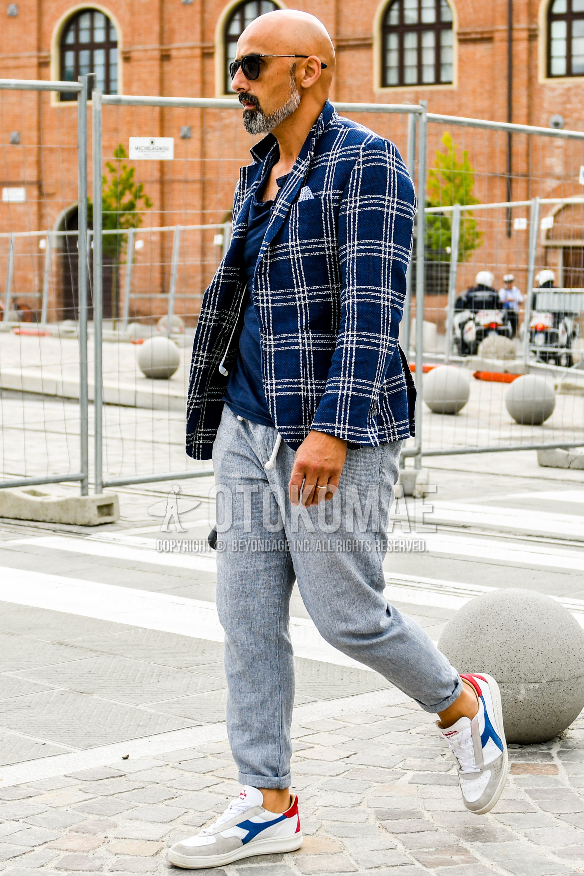 Men's spring summer autumn outfit with plain sunglasses, navy check tailored jacket, navy plain t-shirt, gray plain easy pants, white low-cut sneakers.