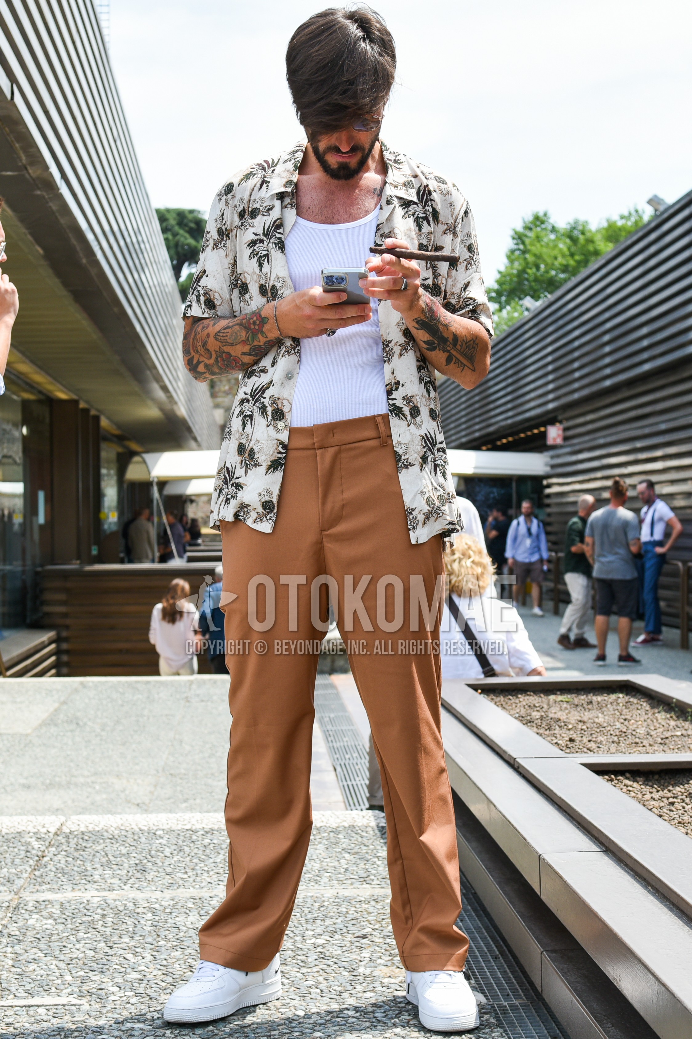 Men's spring summer outfit with black plain sunglasses, beige tops/innerwear shirt, white plain t-shirt, brown plain chinos, white low-cut sneakers.
