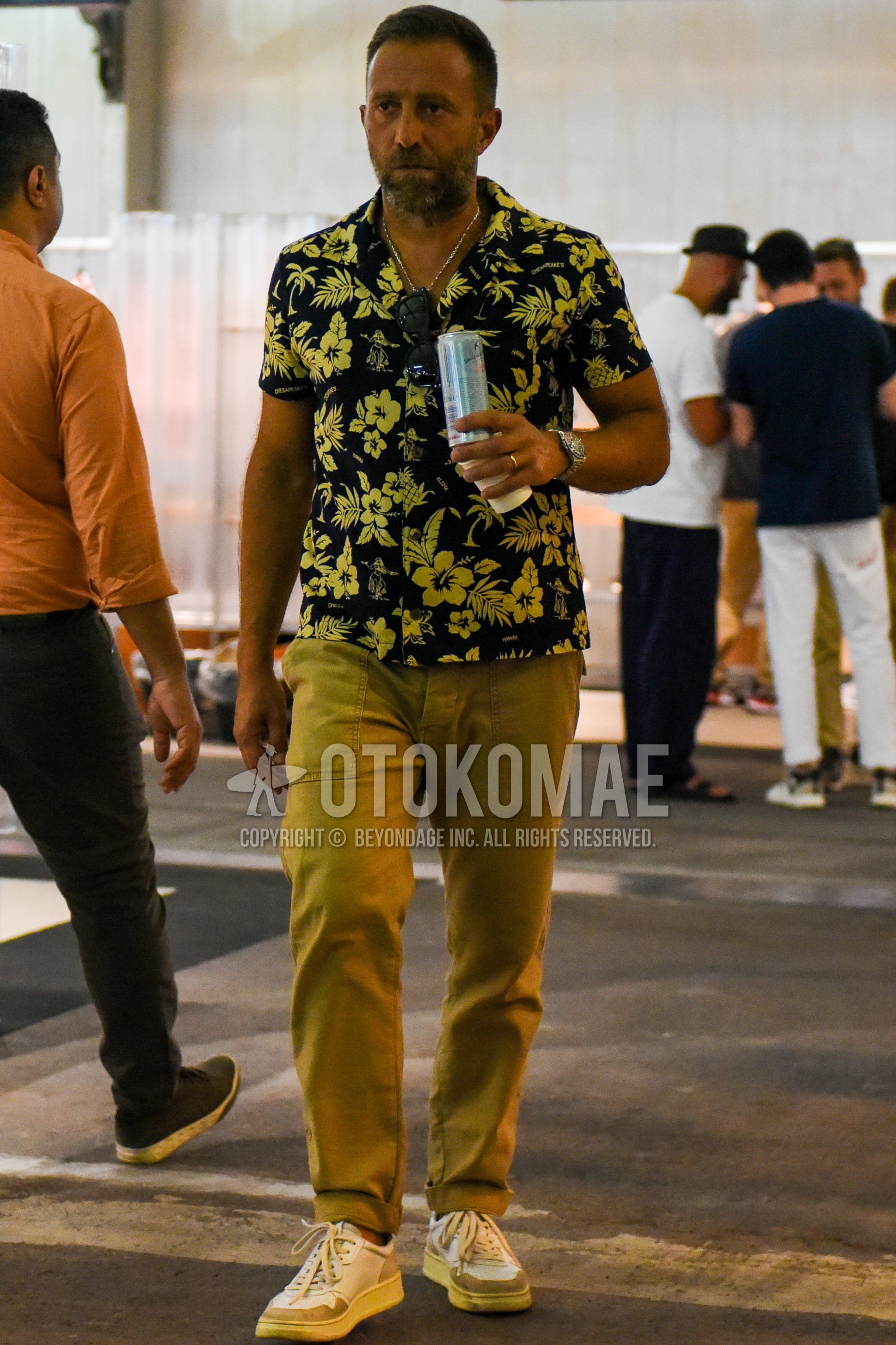 Men's spring summer outfit with yellow navy botanical shirt, beige plain chinos, white low-cut sneakers.