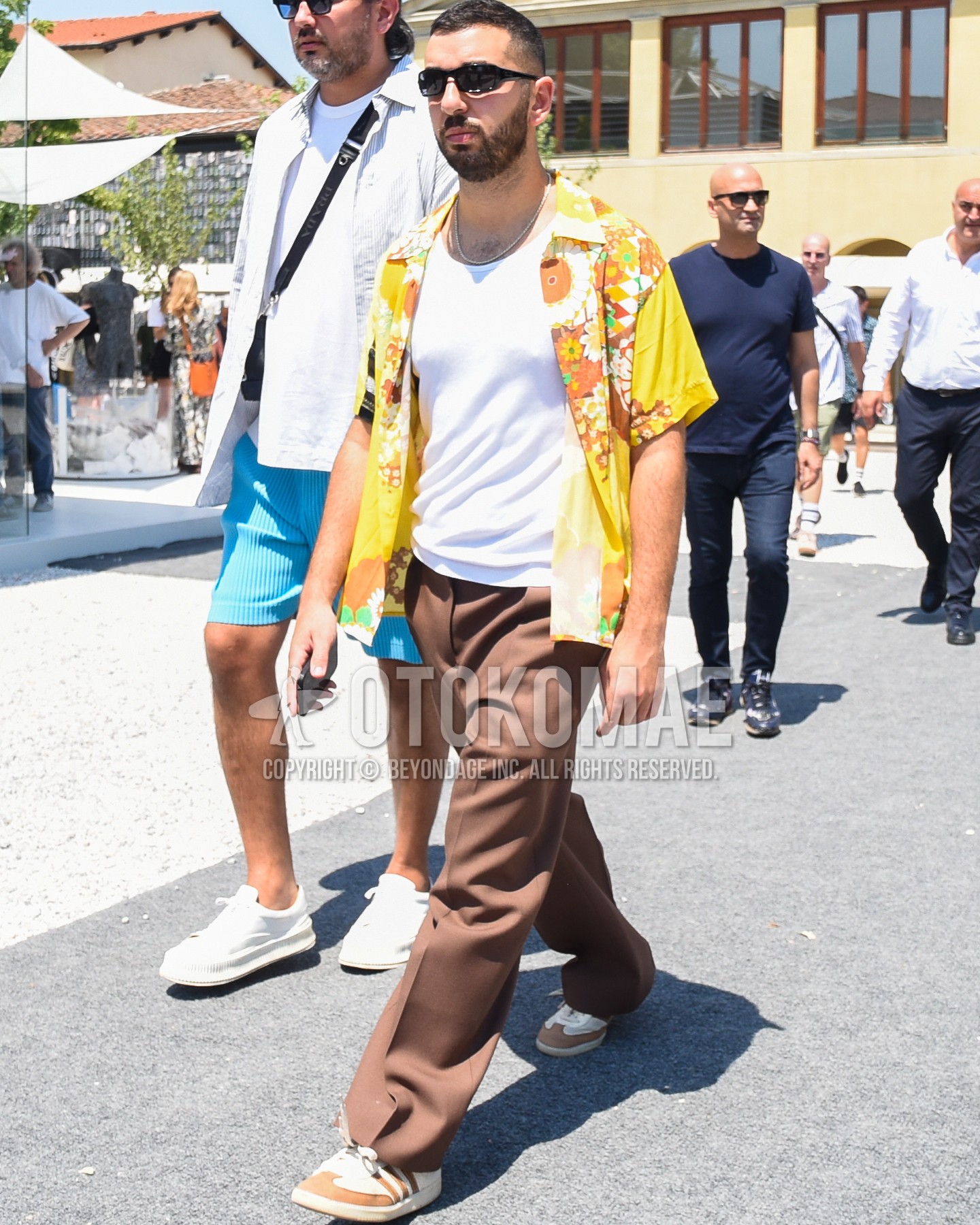 Men's spring summer outfit with black plain sunglasses, white plain tank top, yellow tops/innerwear shirt, brown plain slacks, brown plain wide pants, brown straight-tip shoes leather shoes.