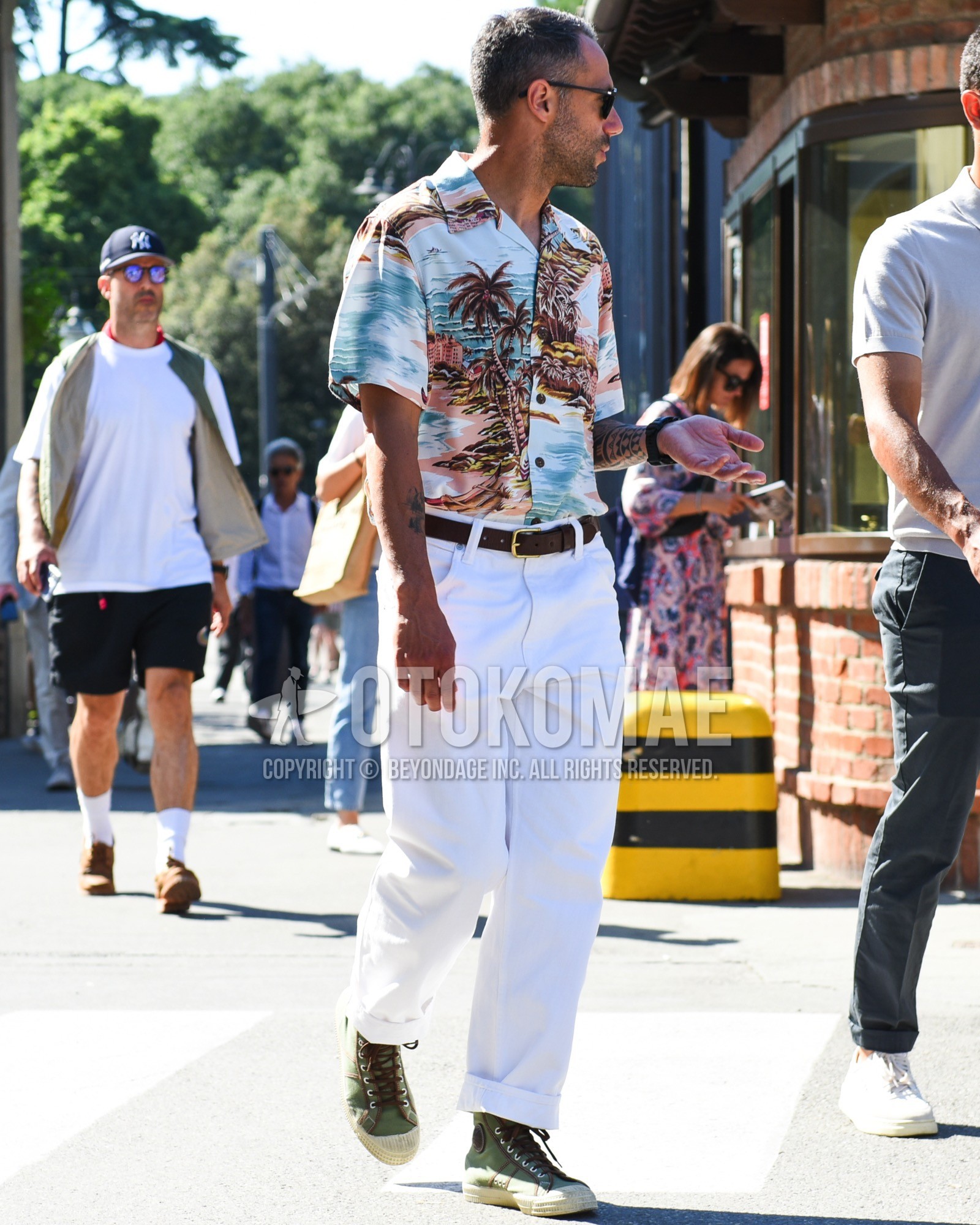 Men's spring summer outfit with black plain sunglasses, white graphic shirt, brown plain leather belt, white plain cotton pants, white plain wide pants, green high-cut sneakers.