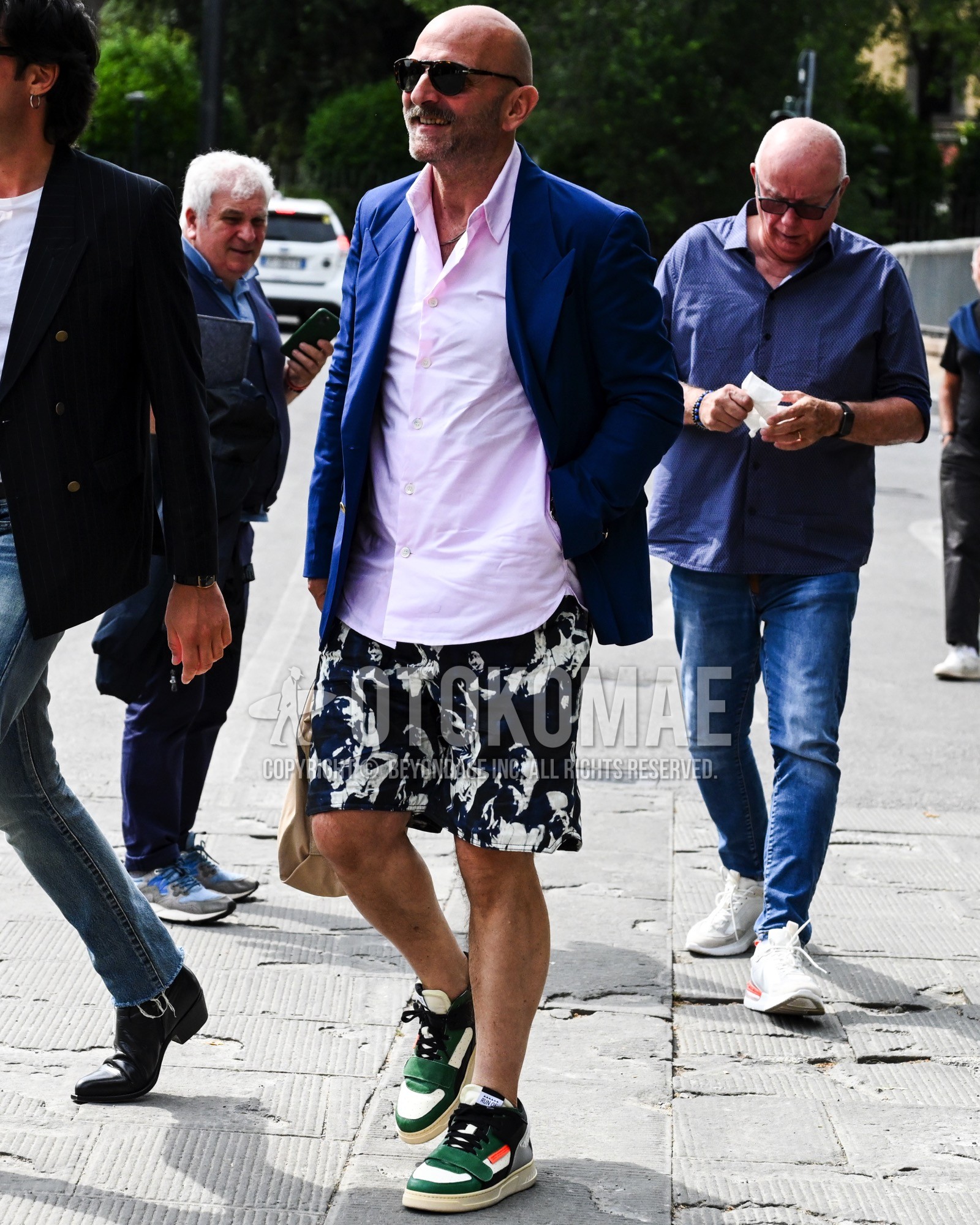 Men's spring summer outfit with black plain sunglasses, navy plain tailored jacket, pink plain shirt, black whole pattern short pants, green low-cut sneakers.