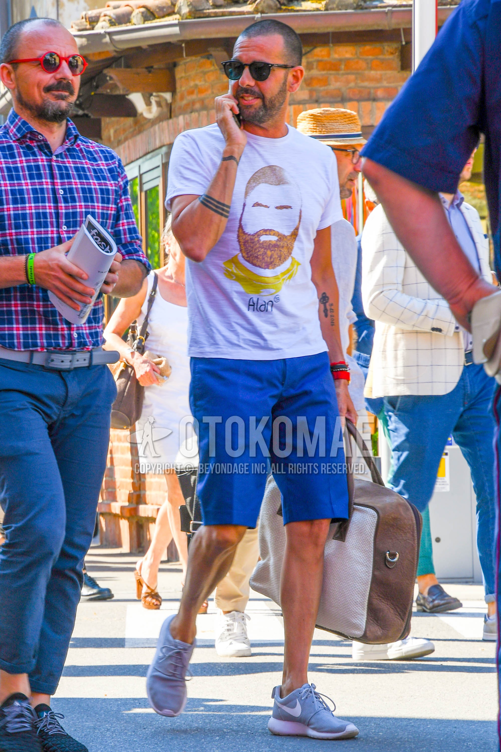 Men's summer outfit with plain sunglasses, white graphic t-shirt, blue plain short pants, gray low-cut sneakers.