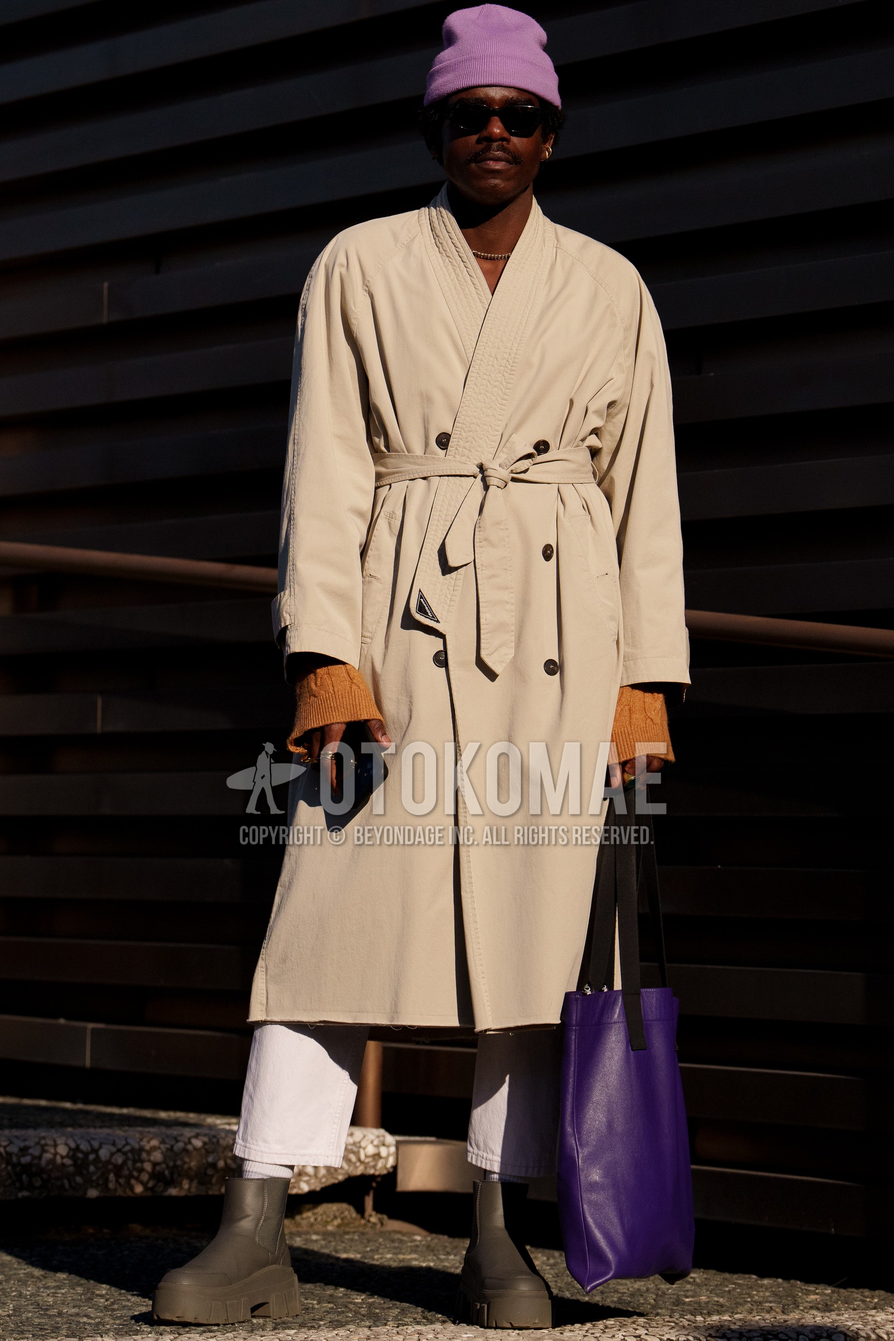 Men's autumn winter outfit with purple plain knit cap, black plain sunglasses, beige plain shawl collar coat, orange plain sweater, white plain cotton pants, white plain socks, olive green side-gore boots, purple plain tote bag.